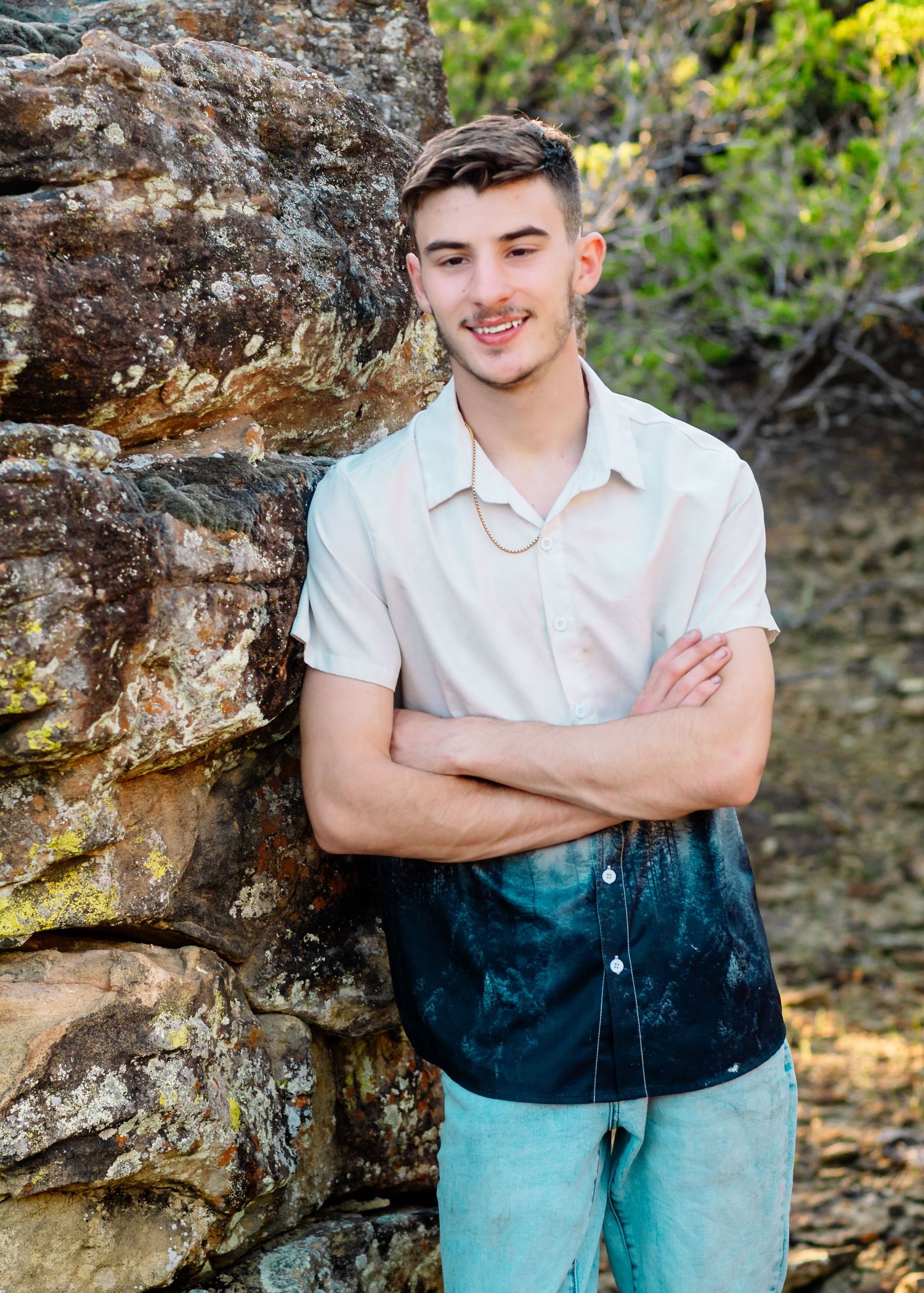 Person in white shirt and gradient blue pants posing against a textured stone wall outdoors.