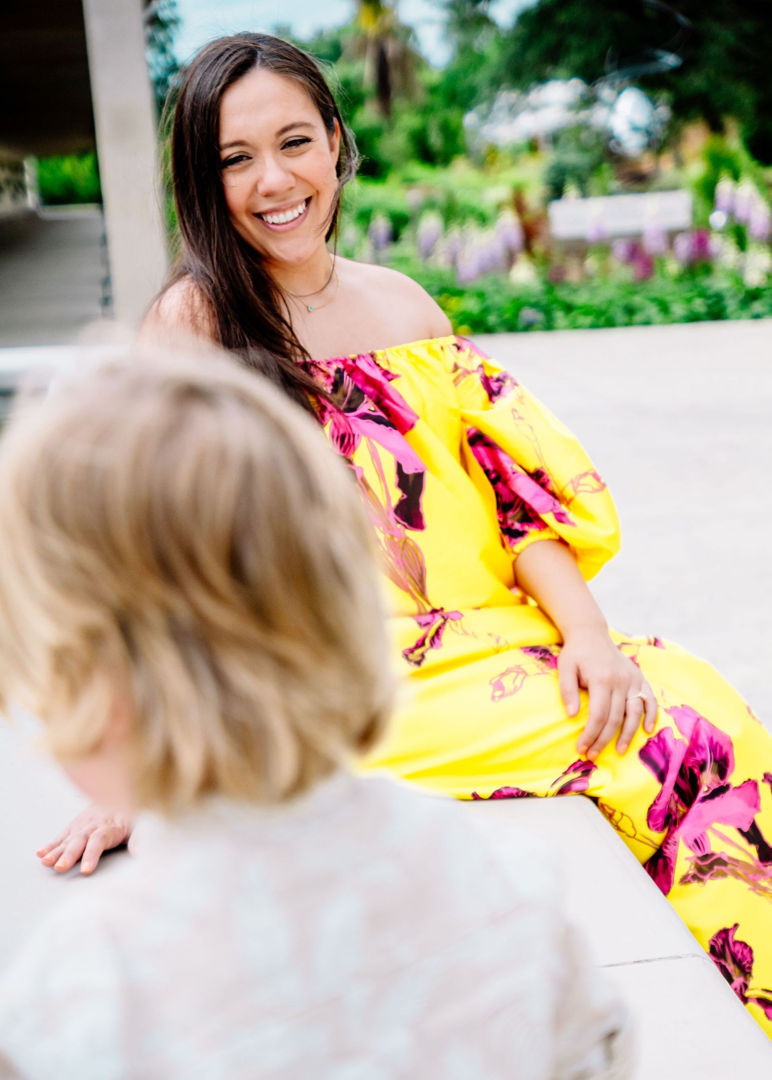 Bright yellow floral dress stands out against garden greenery in outdoor portrait series.