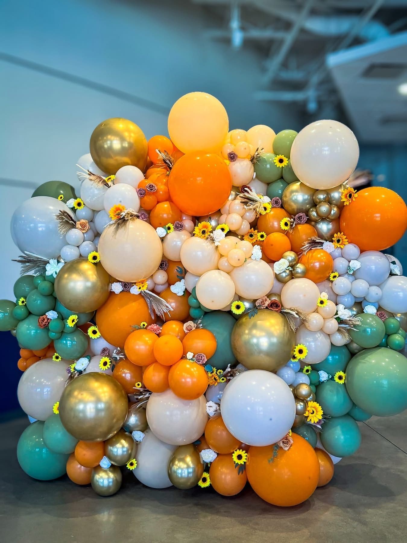 Elegant balloon garland with orange, teal, gold and white balloons accented with small floral details.