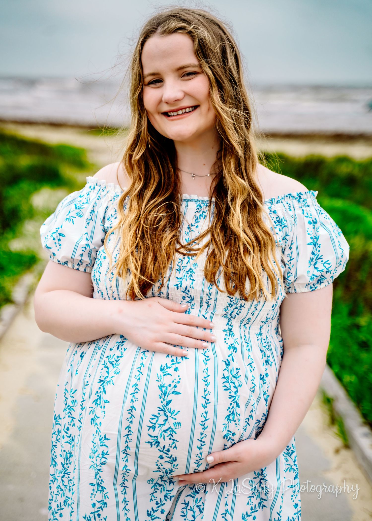 Woman in blue and white striped dress smiles warmly during an outdoor photo session.
