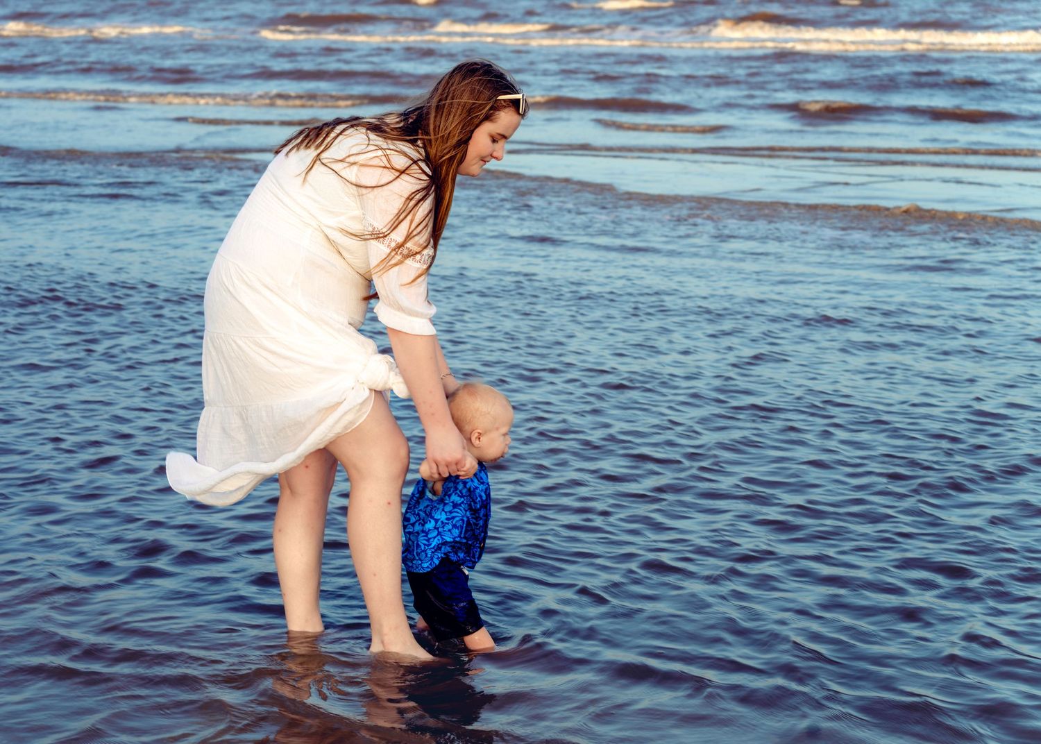 Person in white dress splashes in ocean waves during beach photoshoot.
