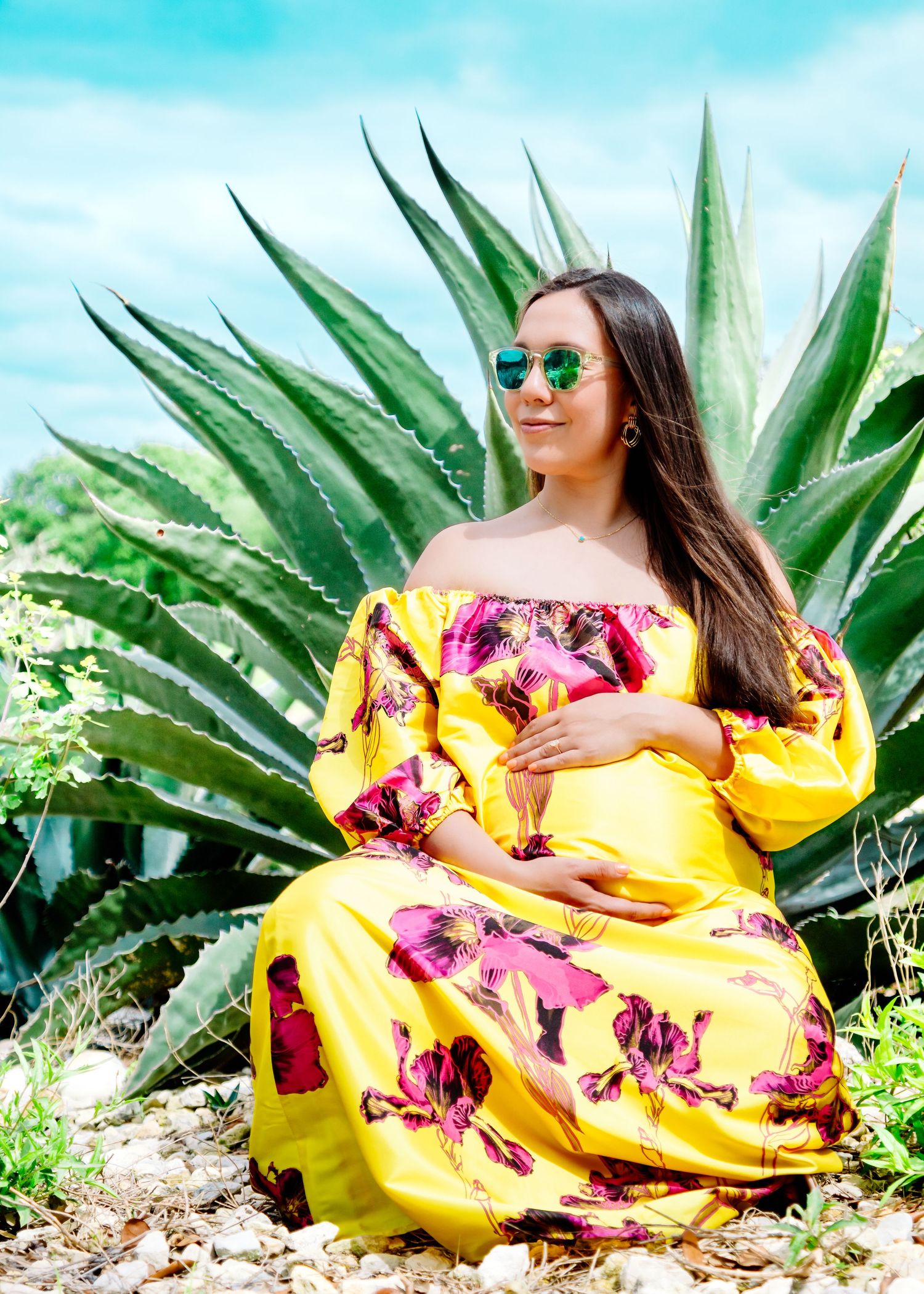 Bright maternity photoshoot with yellow dress against blue sky and agave plants.