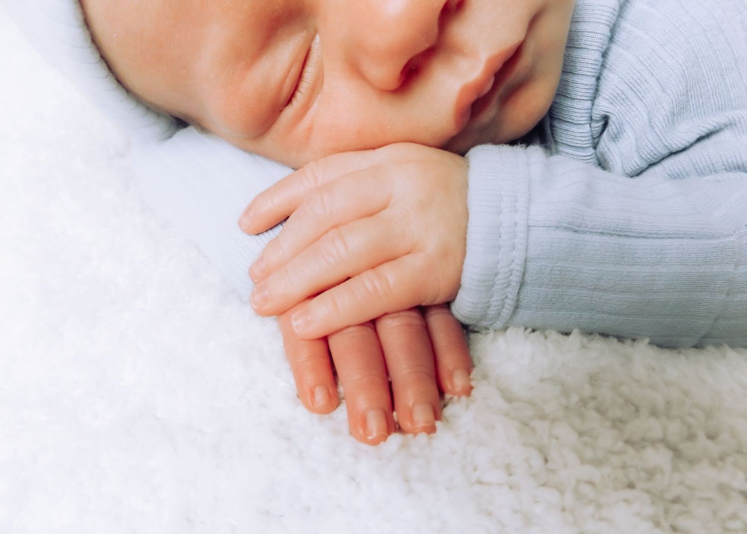 Close-up of a sleeping baby's hands folded peacefully on white fabric.