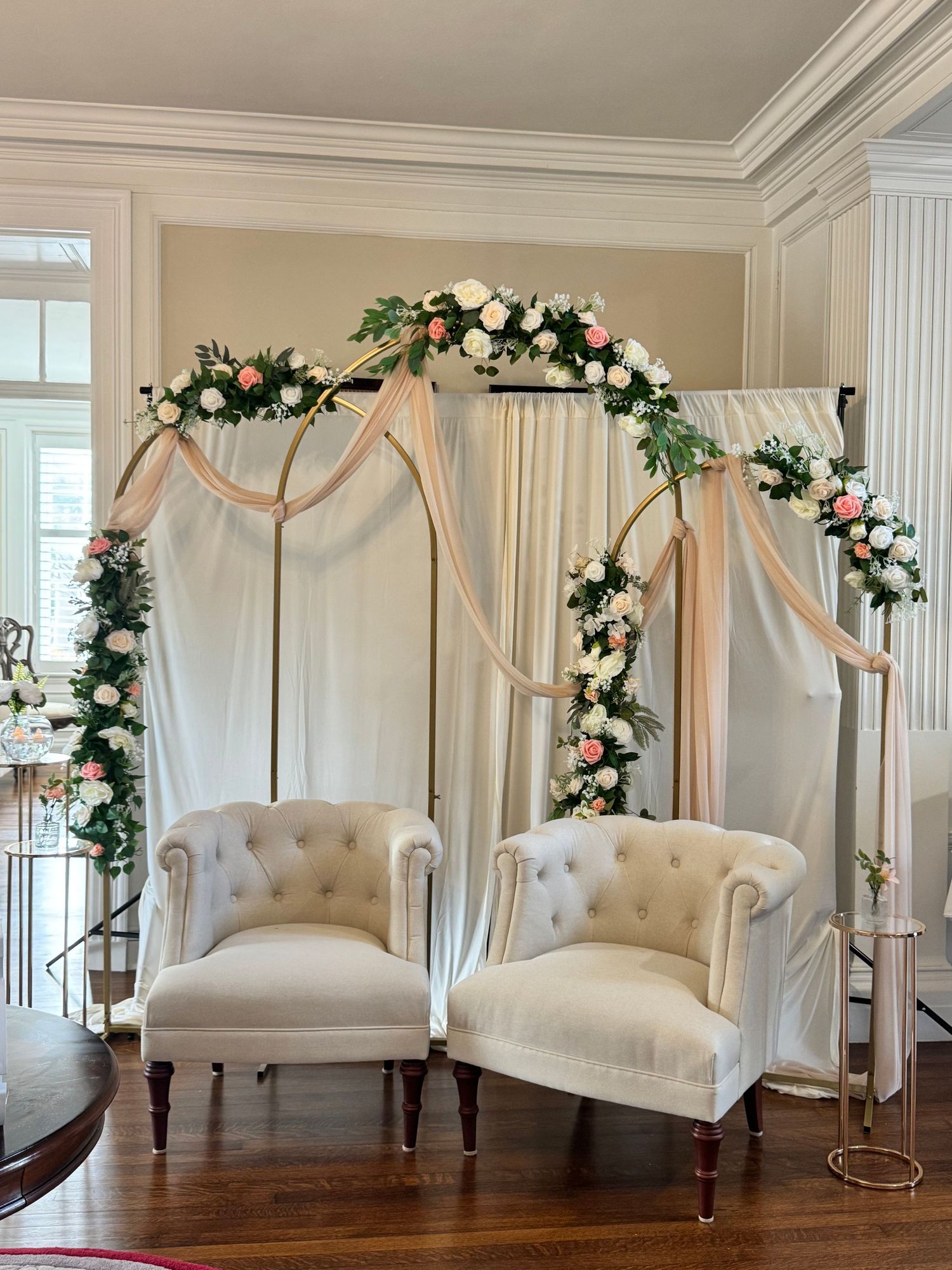 Elegant white chairs with floral arches create a romantic indoor wedding ceremony setup.