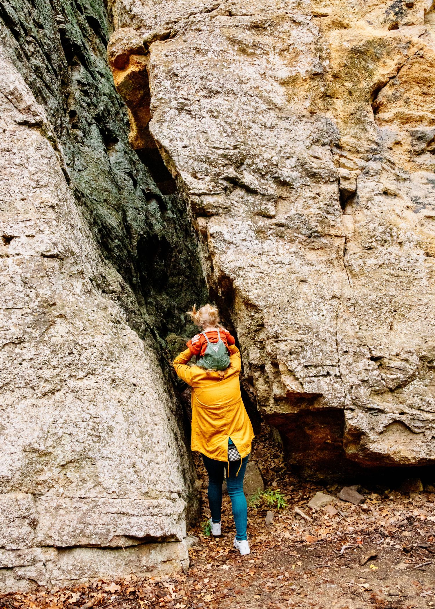Child in yellow top exploring a rocky cave formation in nature.