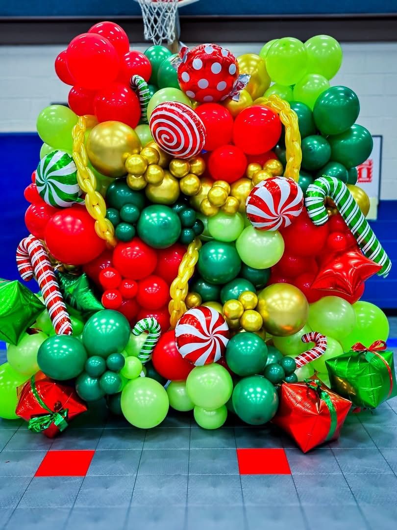 Christmas-themed balloon garland with red, green and gold ornaments against blue wall.