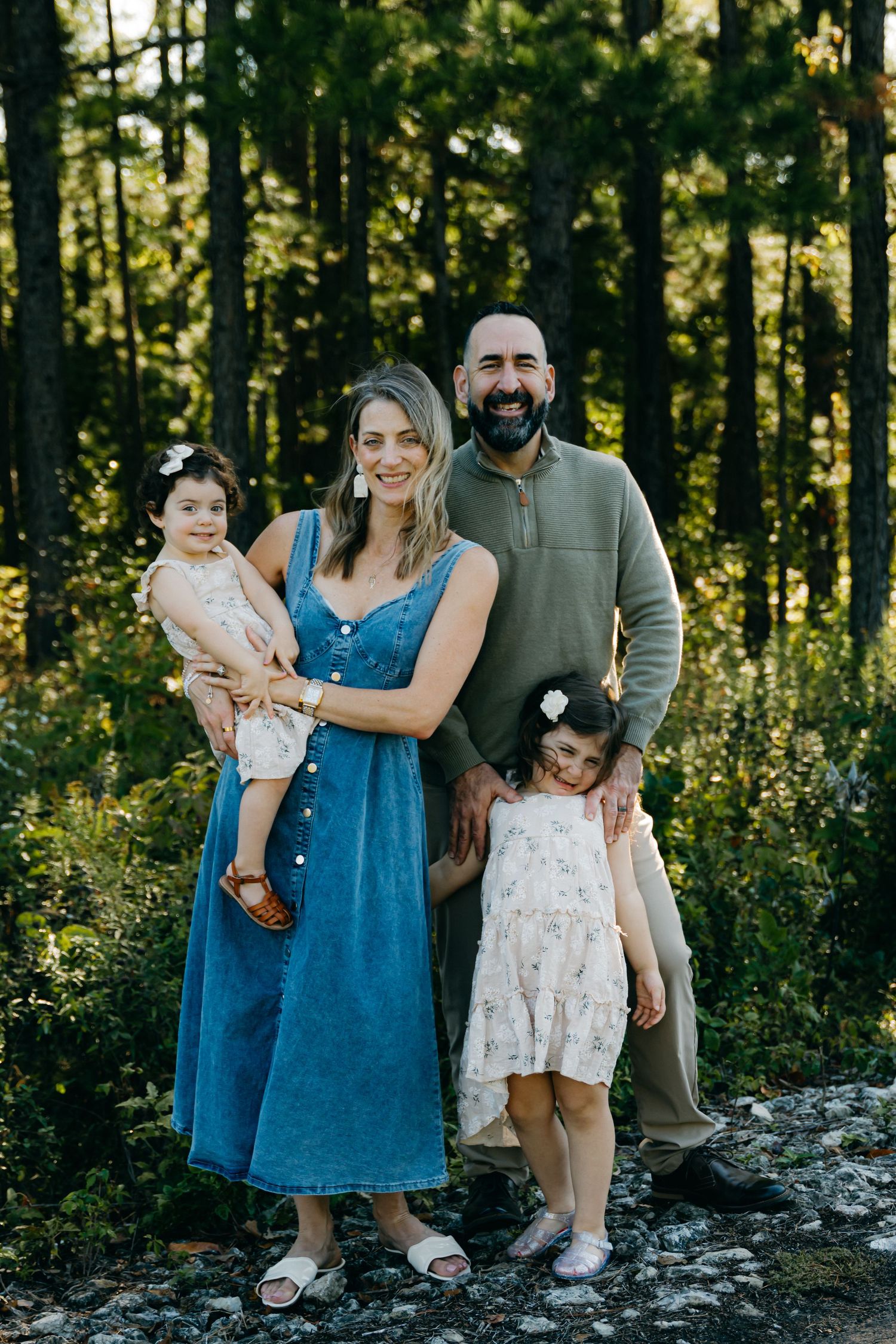 A casual family portrait in a forest setting with coordinated blue and neutral outfits.