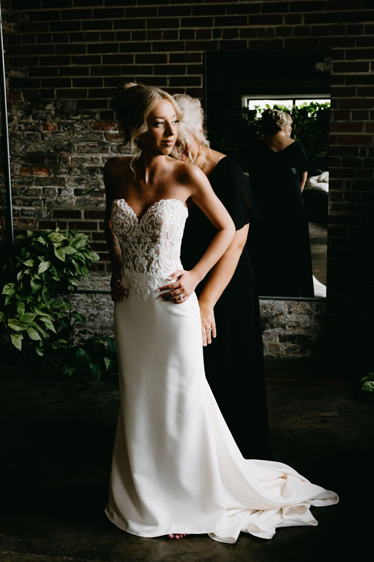 Dramatic lighting captures bride in flowing white dress against brick wall.