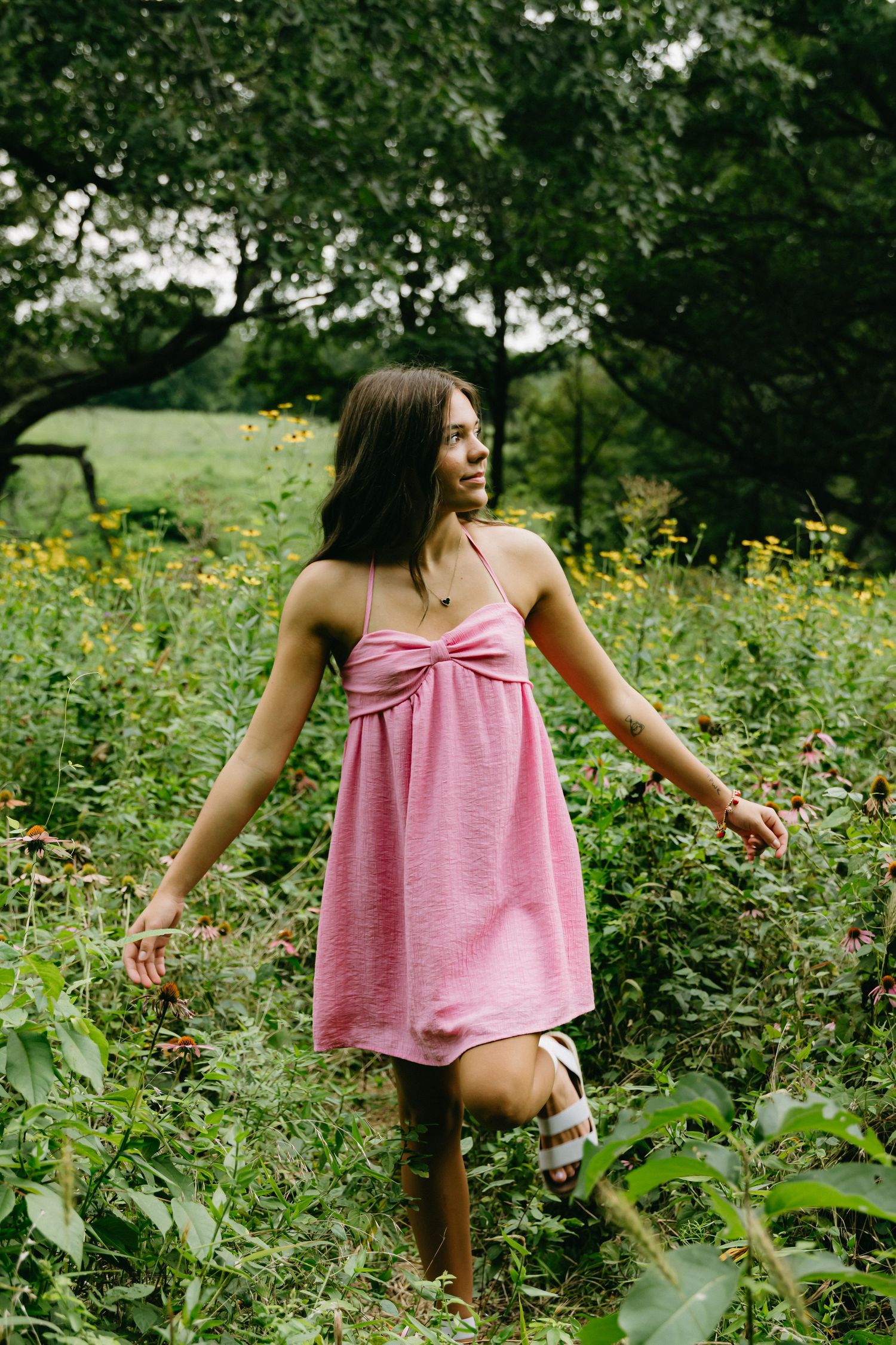 Person in pink tank top explores wildflower garden with yellow blooms.