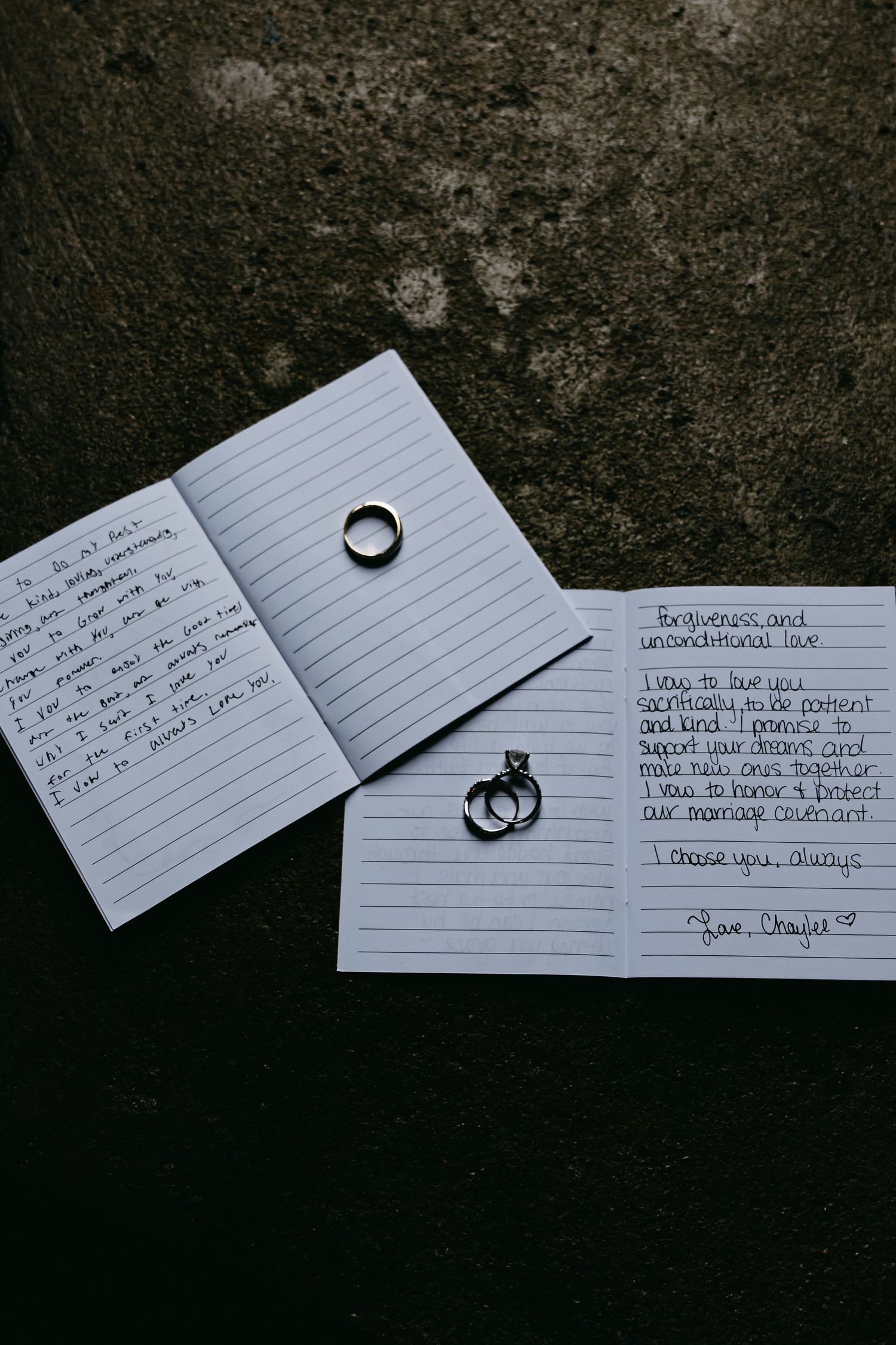 Wedding rings rest on handwritten note cards against dark background.
