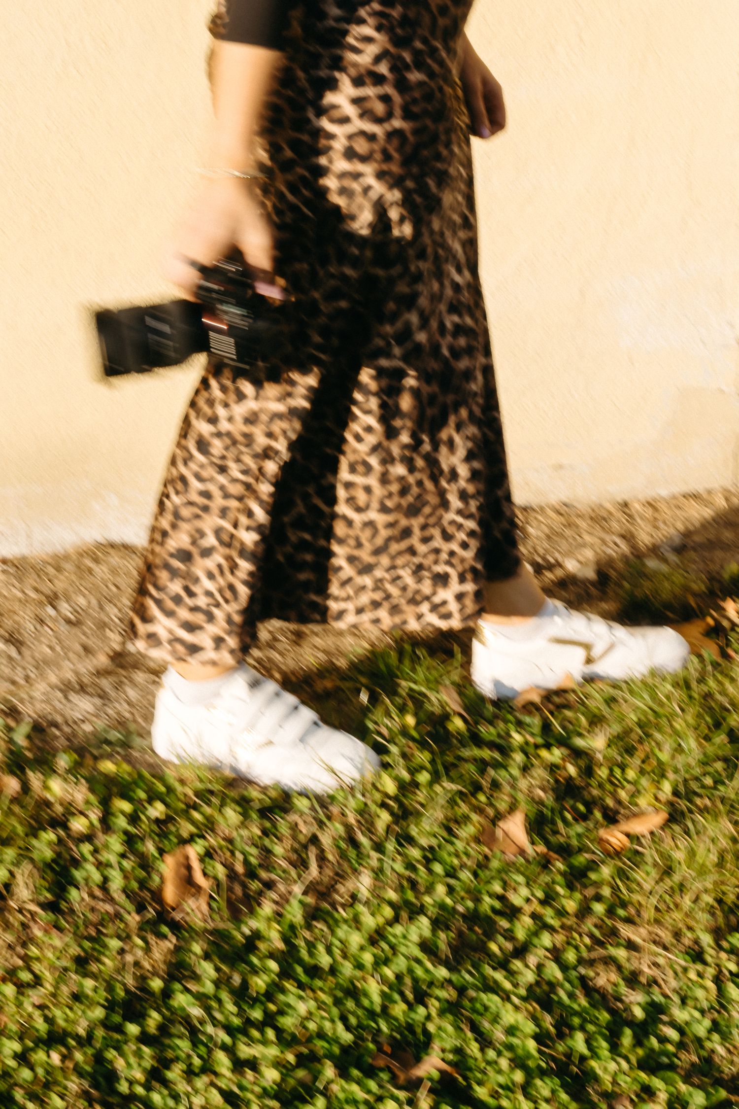 Close-up of leopard print skirt and white sneakers against beige wall.
