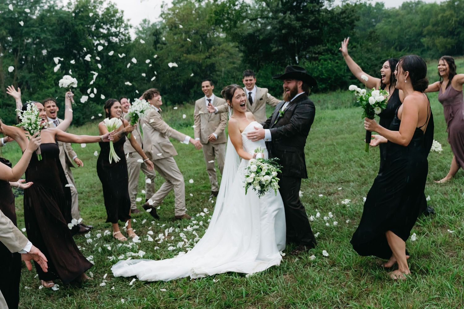 Wedding party celebrates joyfully on a grassy hill during an outdoor summer ceremony.