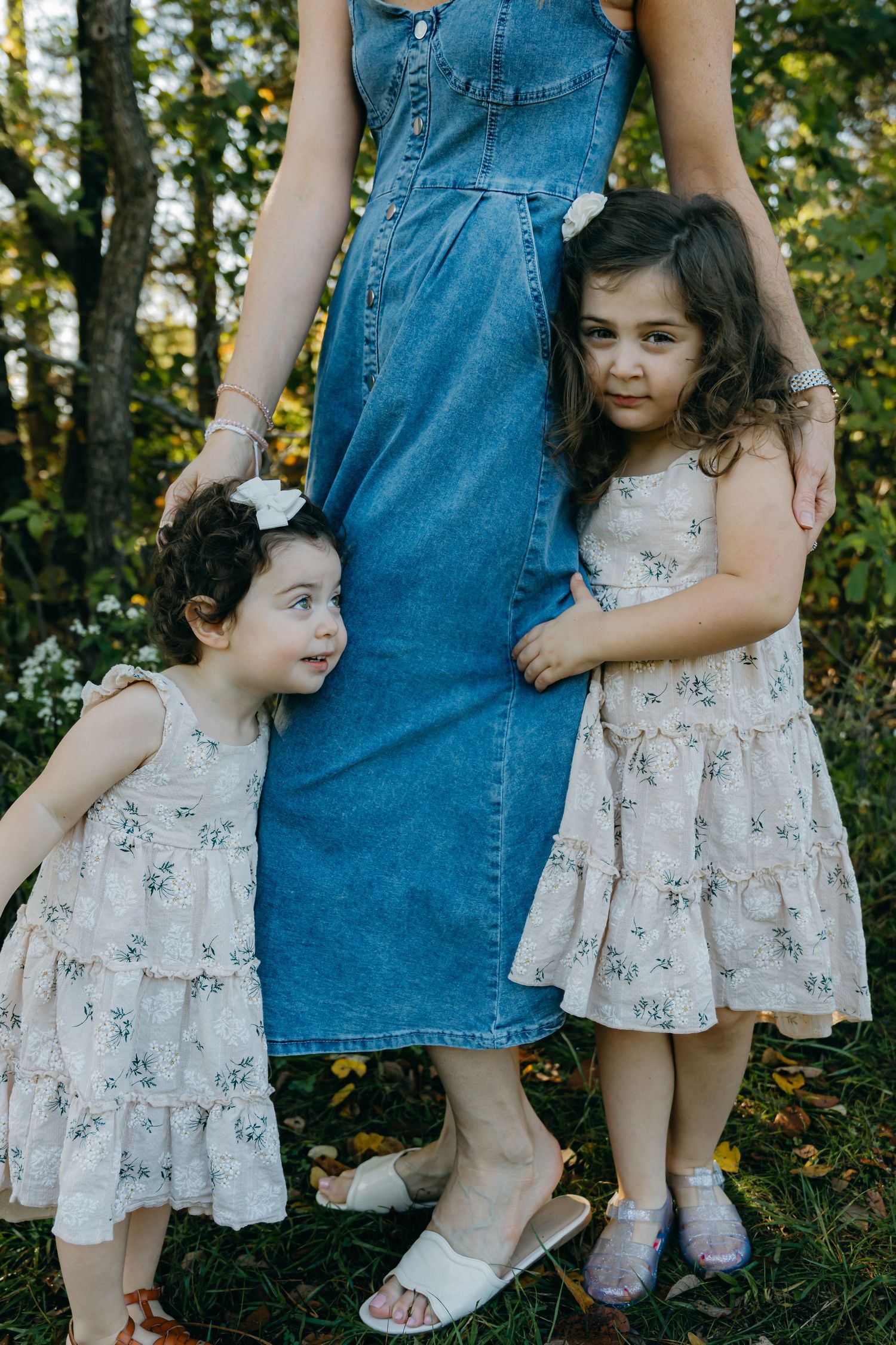 Children in floral dresses stand next to someone wearing denim.