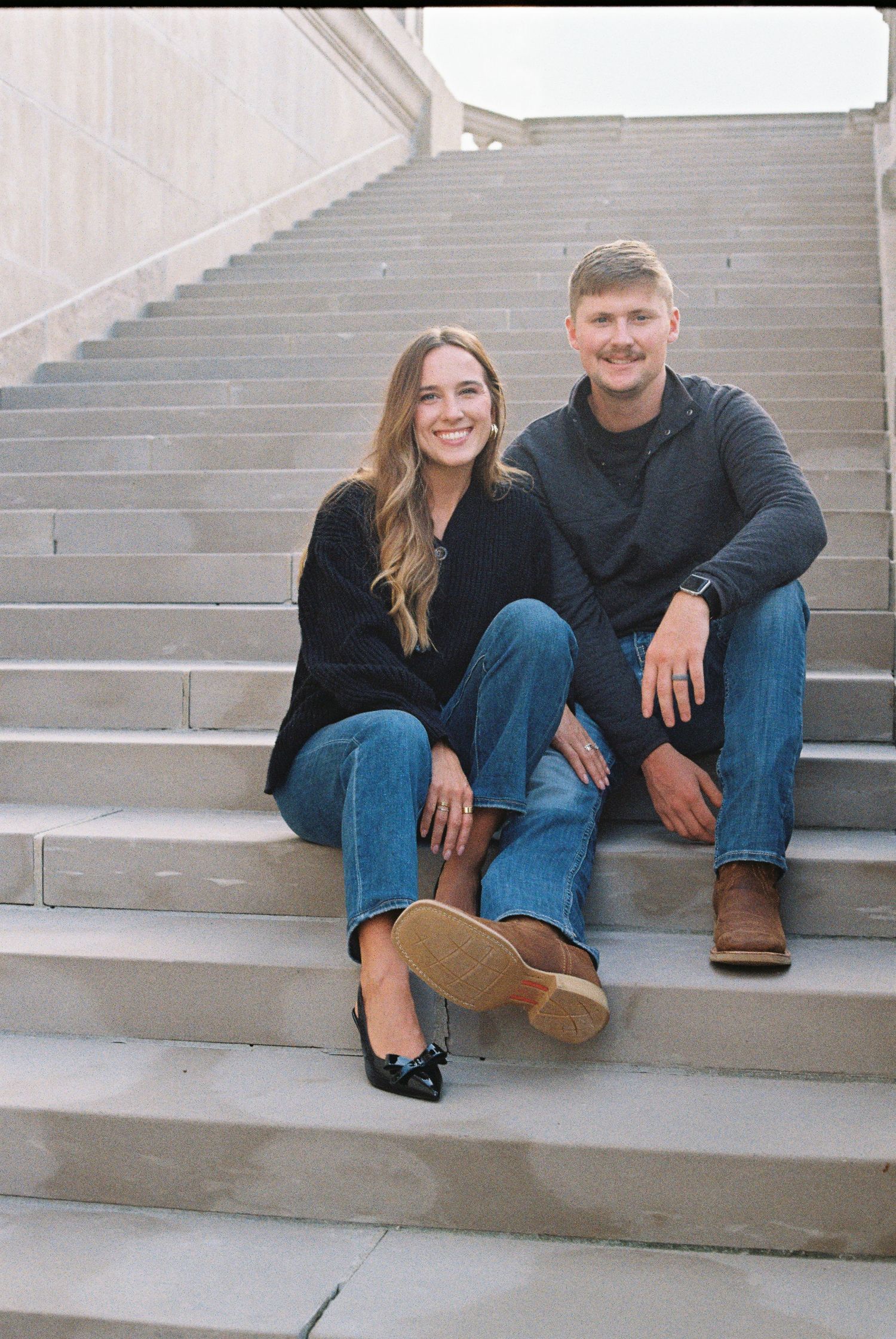 Couple sits casually on concrete steps during outdoor photoshoot.