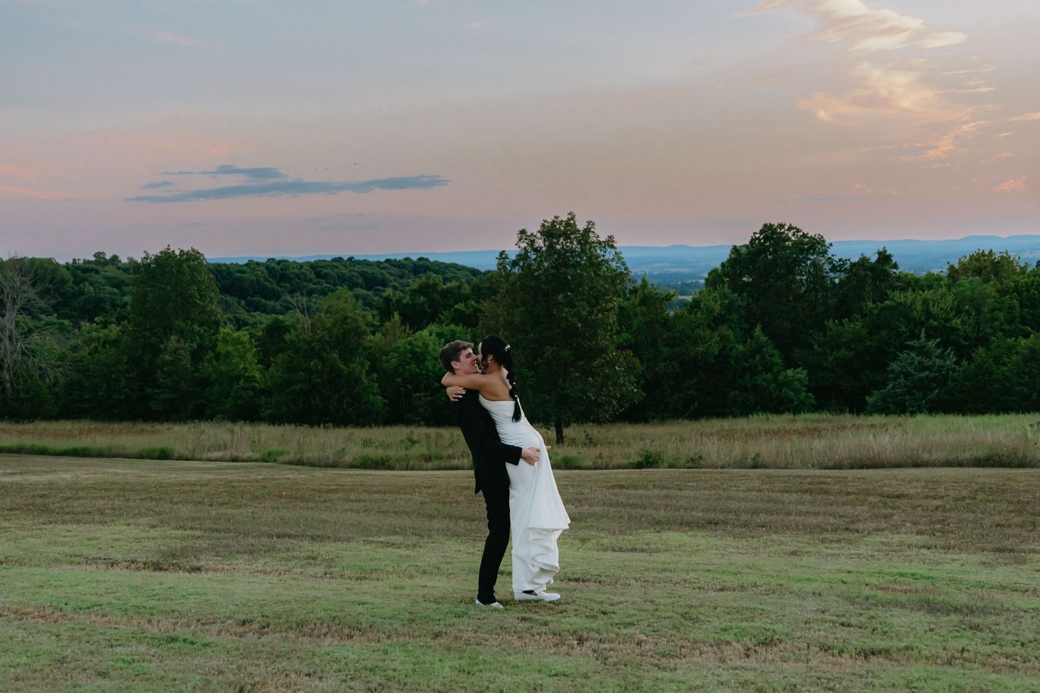 A couple shares an intimate moment in a scenic field during golden hour.