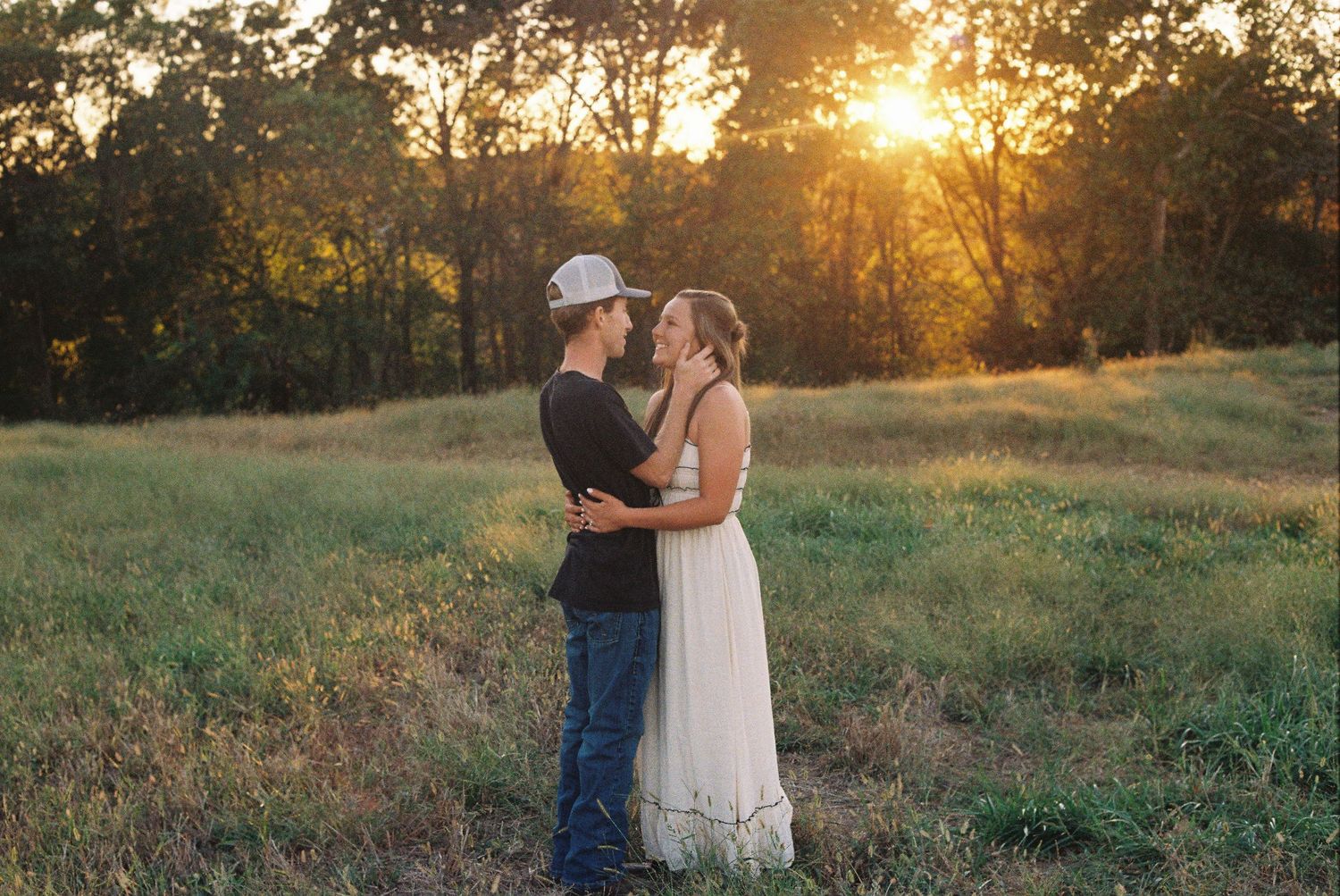Romantic sunset embrace in a rustic field with golden light filtering through trees.