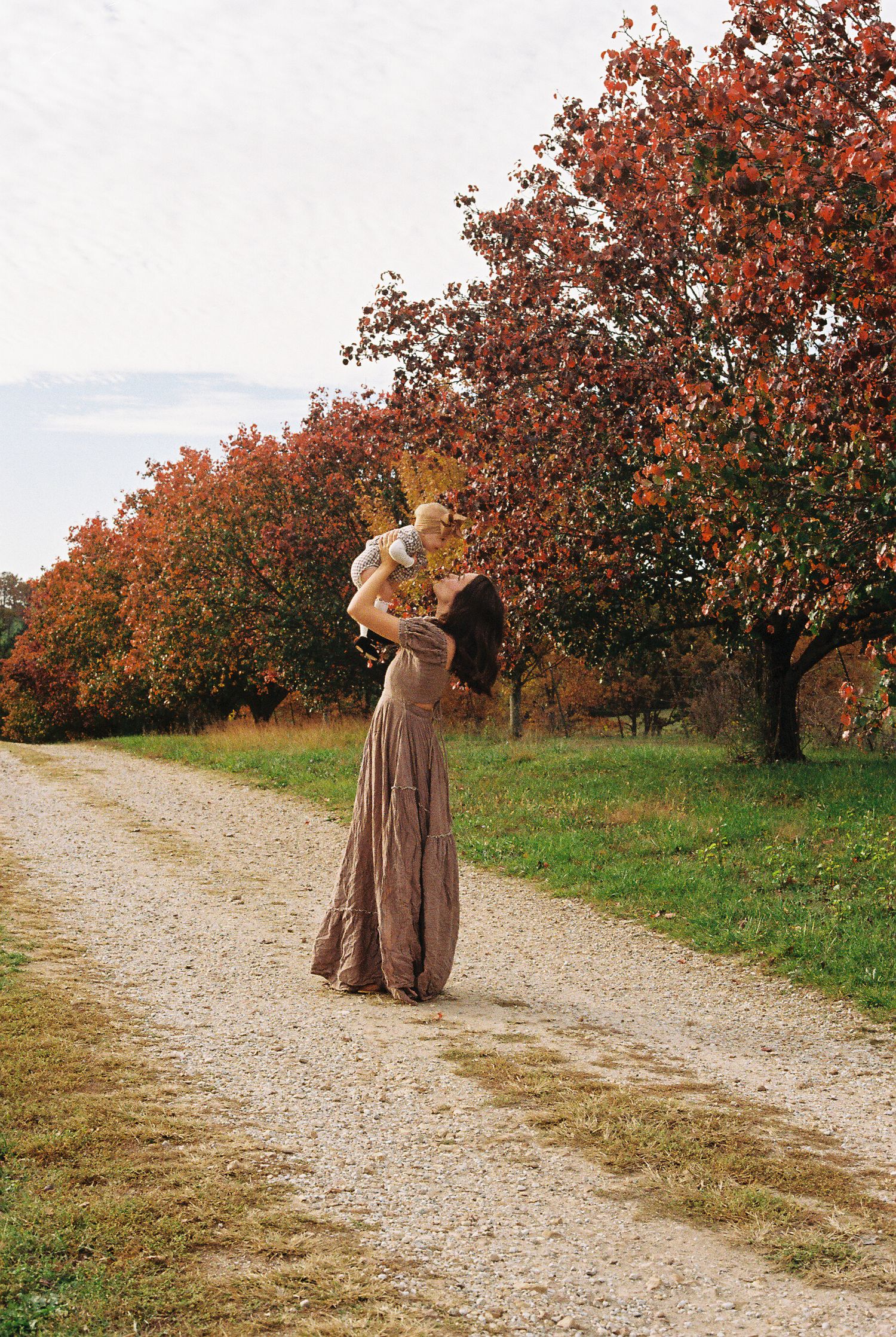 Long brown dress silhouetted against autumn trees on a country path at sunset.