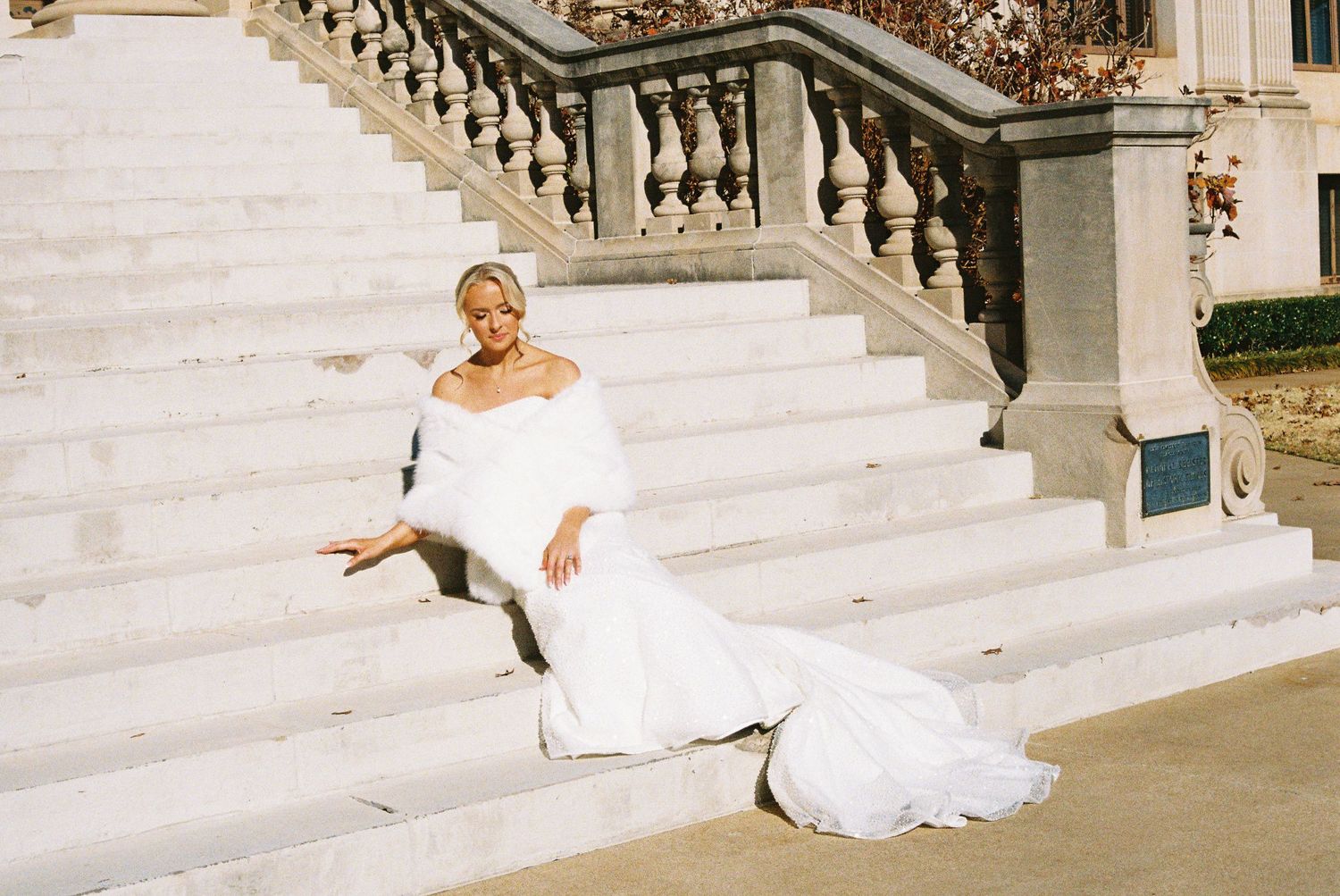 Elegant bride in a flowing white dress poses gracefully on grand marble steps of a historic building.