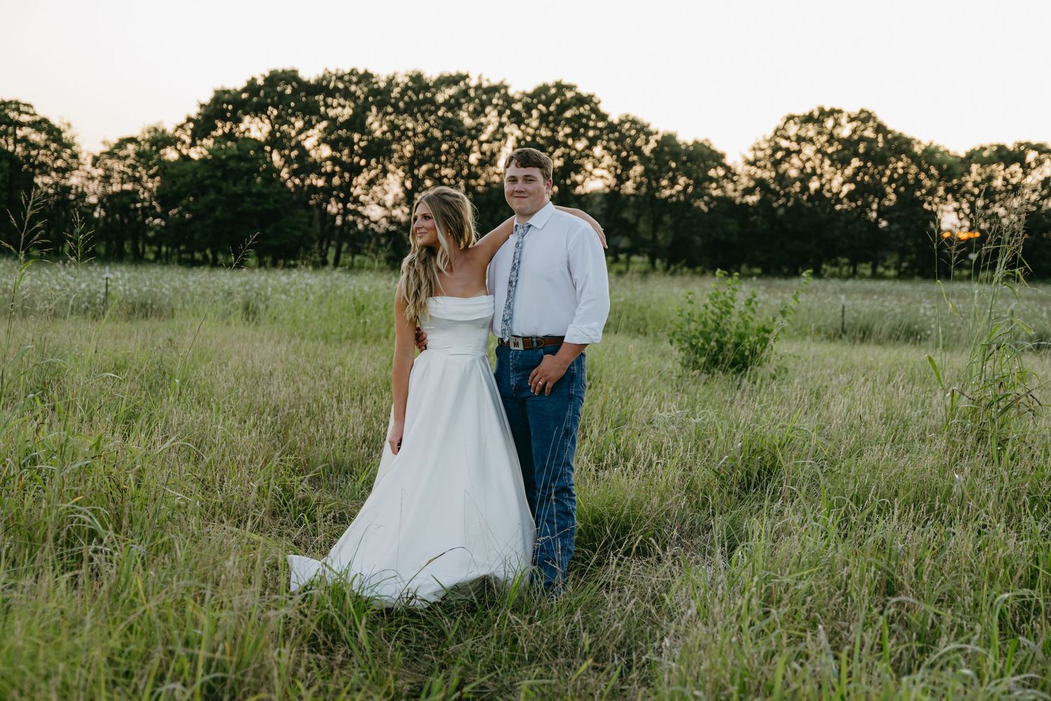 Couple walking through a sunlit meadow during golden hour.