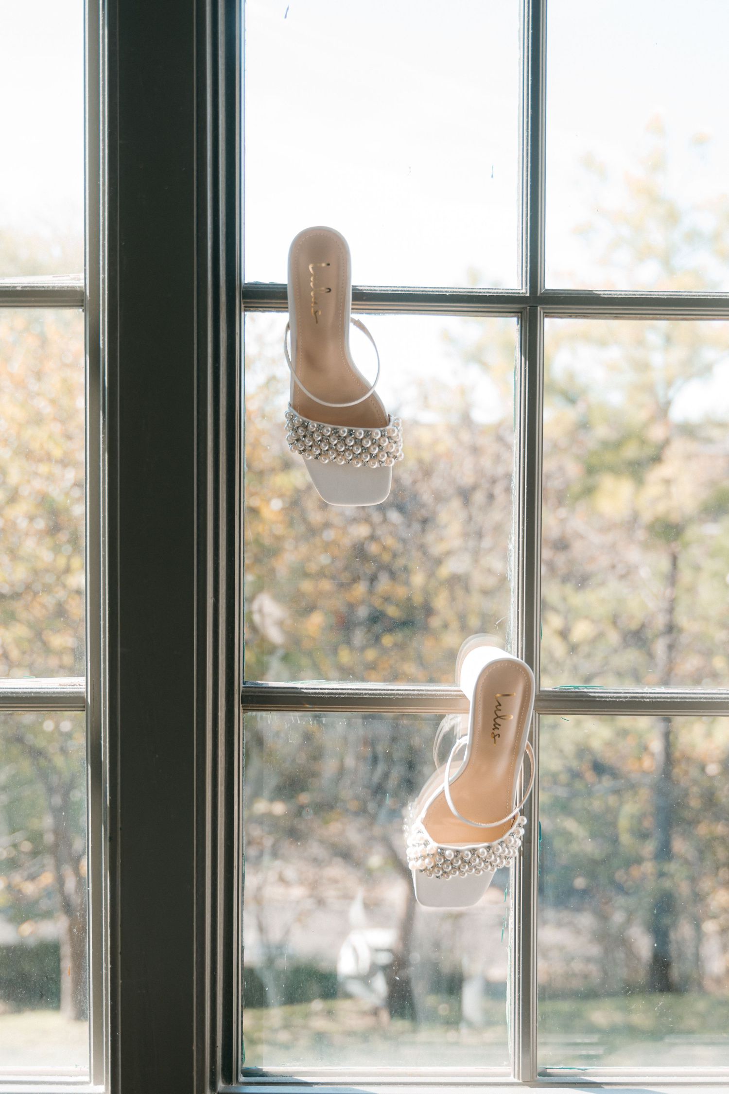 White wedding shoes displayed on a windowsill with natural light.