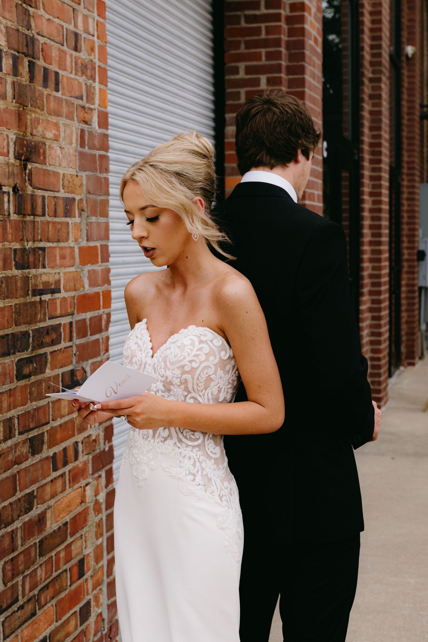 Intimate wedding moment captured against rustic brick wall backdrop.