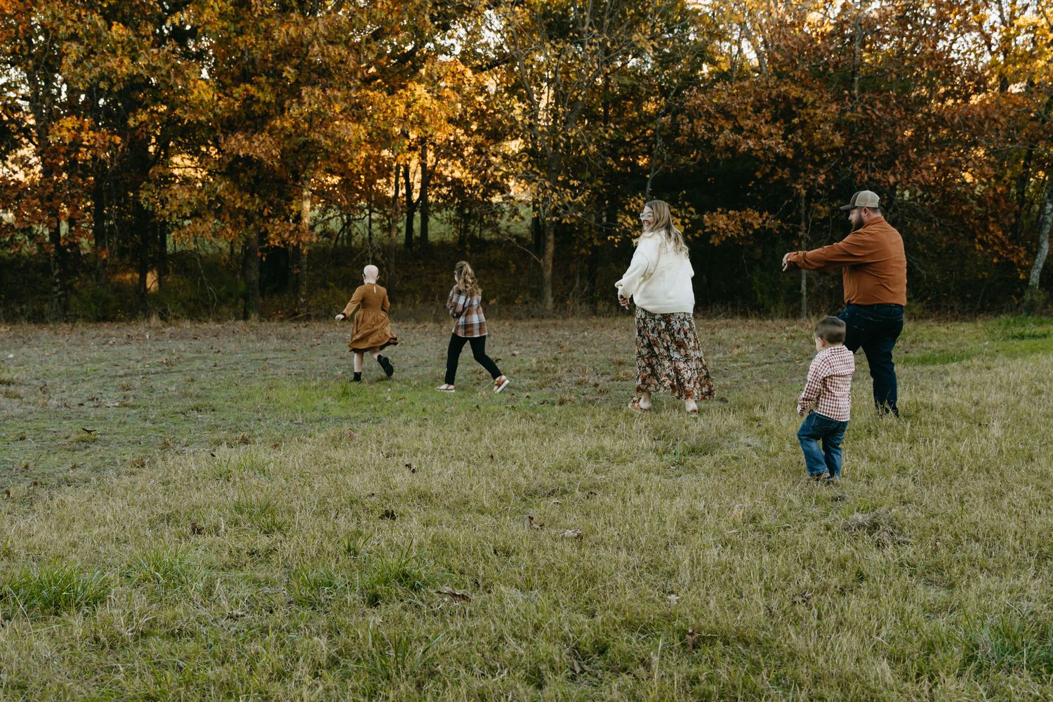 Family walks together across autumn field during golden hour photoshoot.