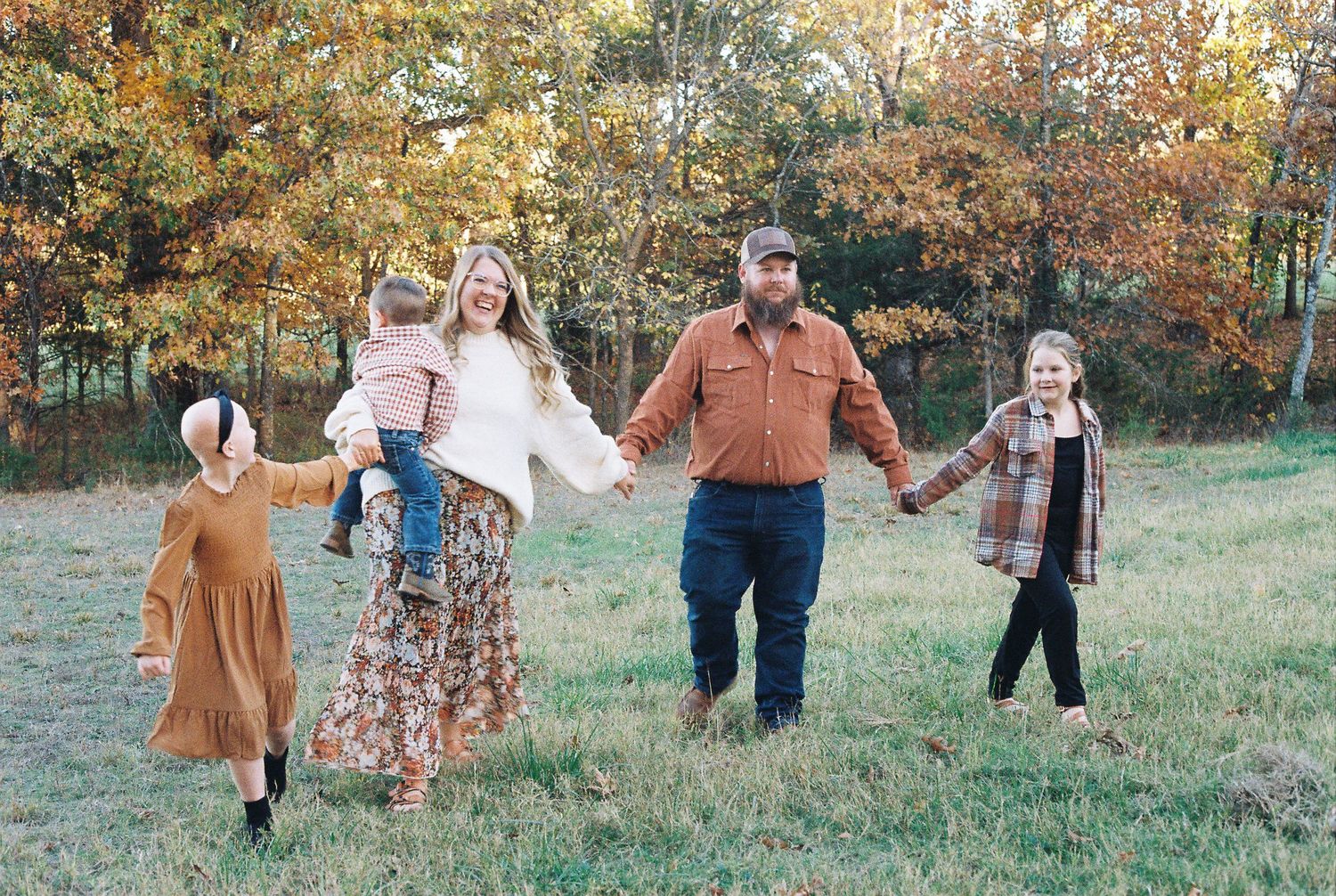 Family walking together hand in hand through autumn field.