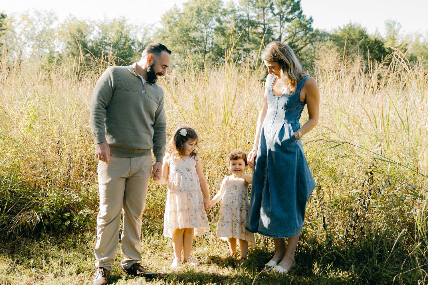Family members walk together through a sunlit field of tall grass.