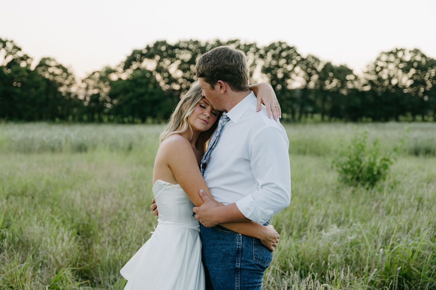 Romantic couple embraces in rustic field setting during golden hour.