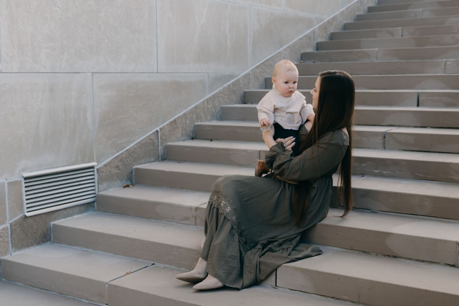 A tender parenting moment captured on concrete stairs in an indoor setting.