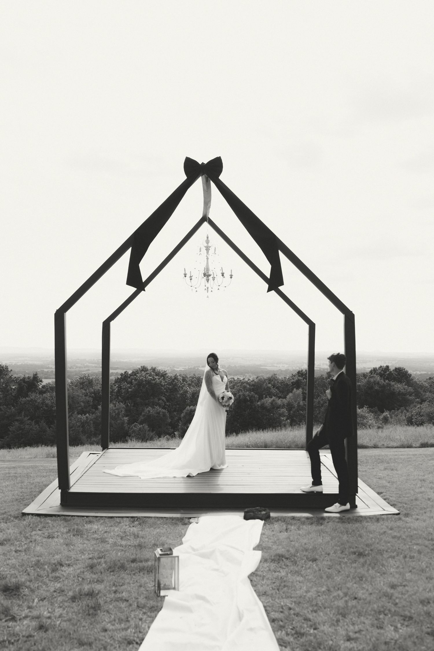 A series of black and white photos showing a wedding ceremony setup with a wooden arch frame on an outdoor hilltop.