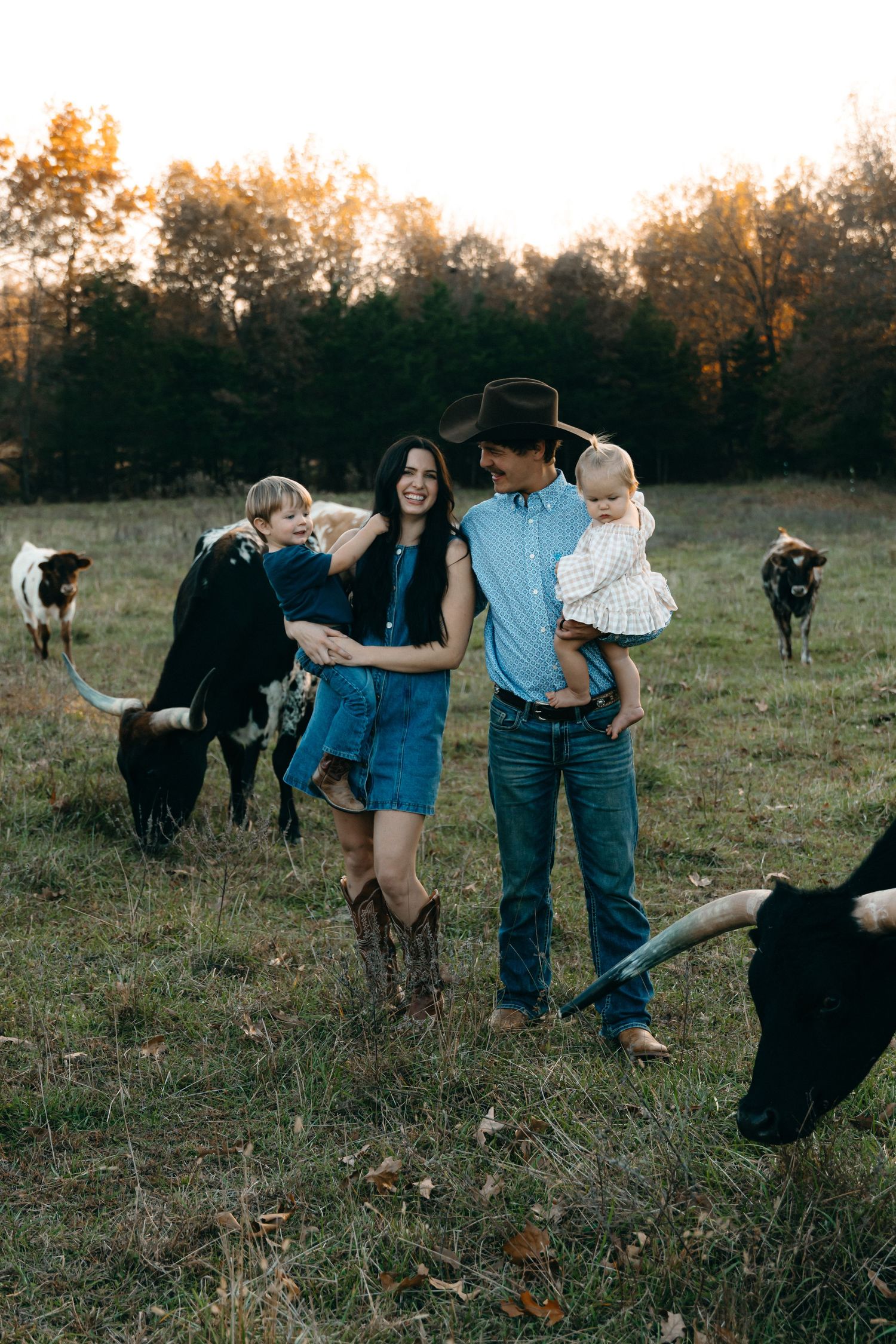 A family poses in a field at sunset with grazing cattle in the background.