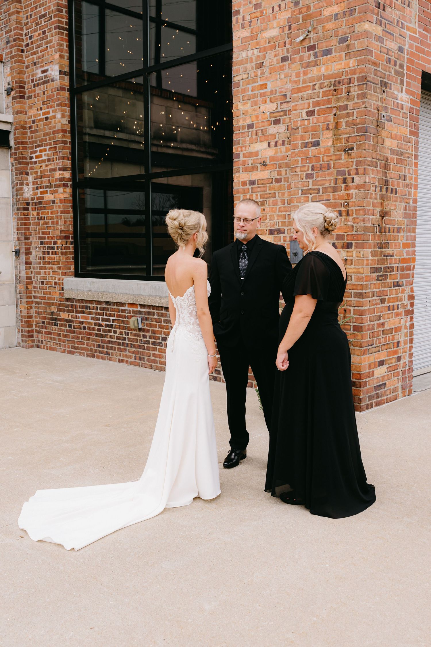 Wedding party gathers outside brick building for intimate moment.