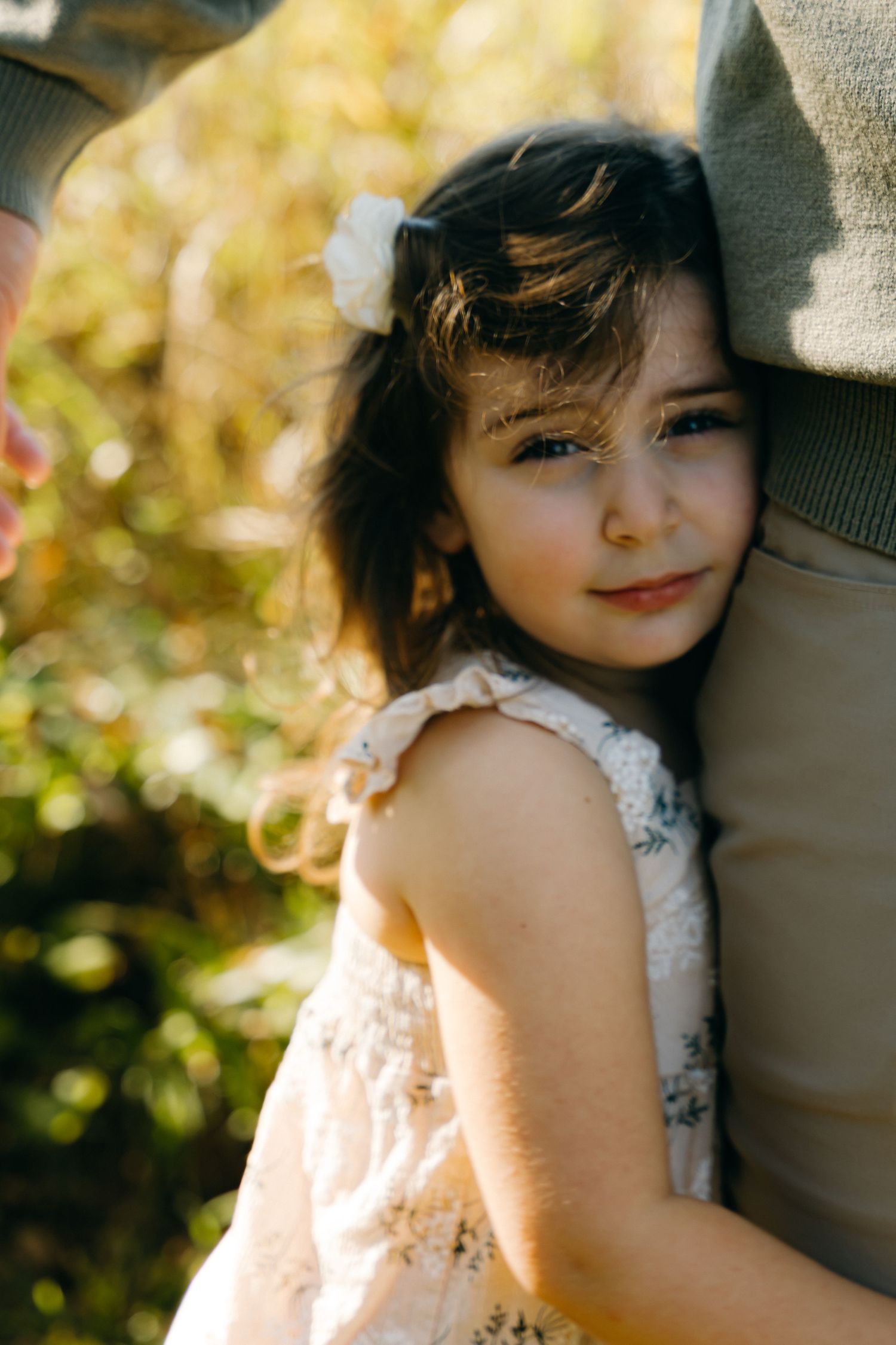 A young child in a lace dress smiles in warm sunlight.