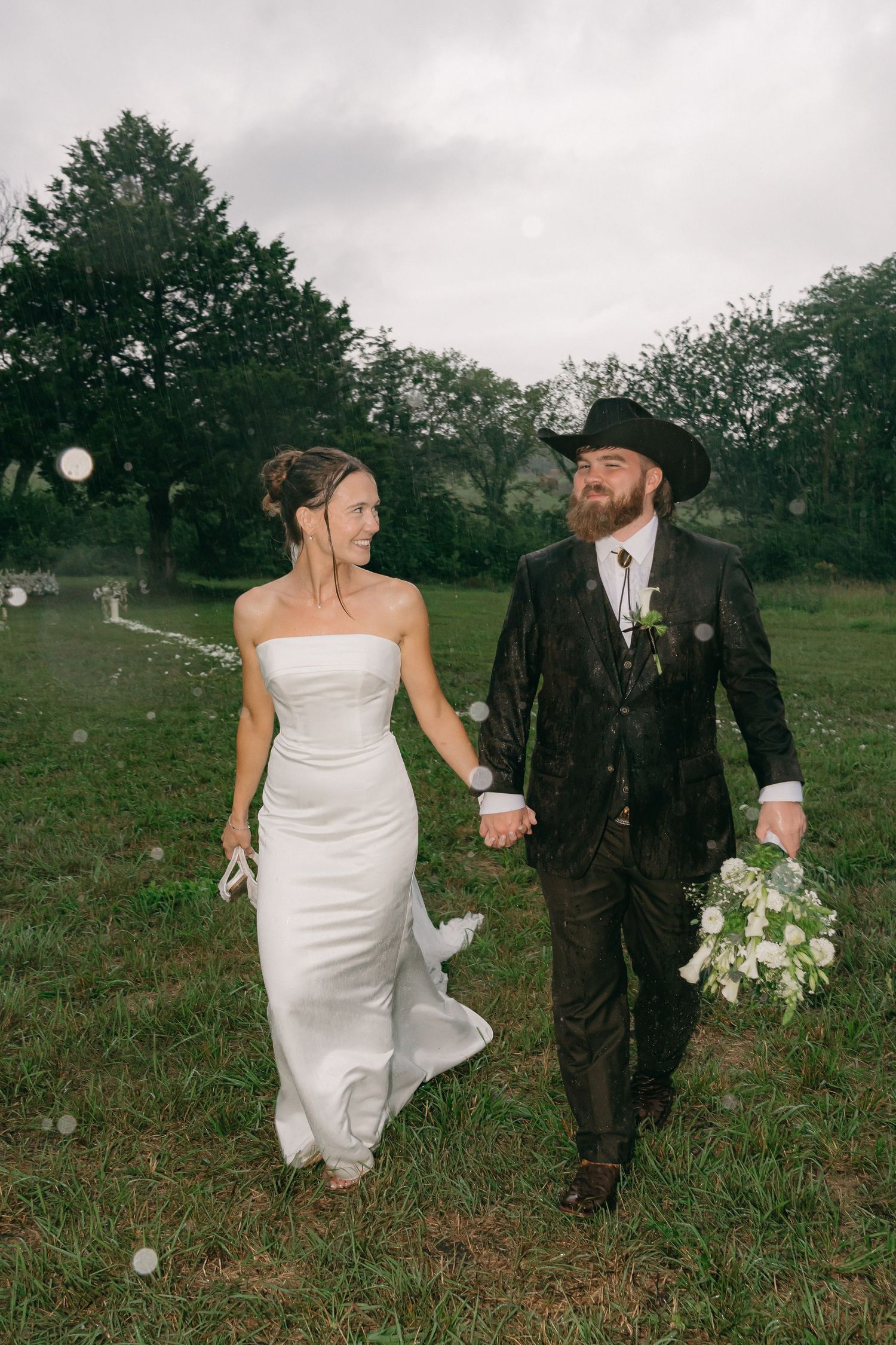 Couple walks hand in hand through a meadow in wedding attire.