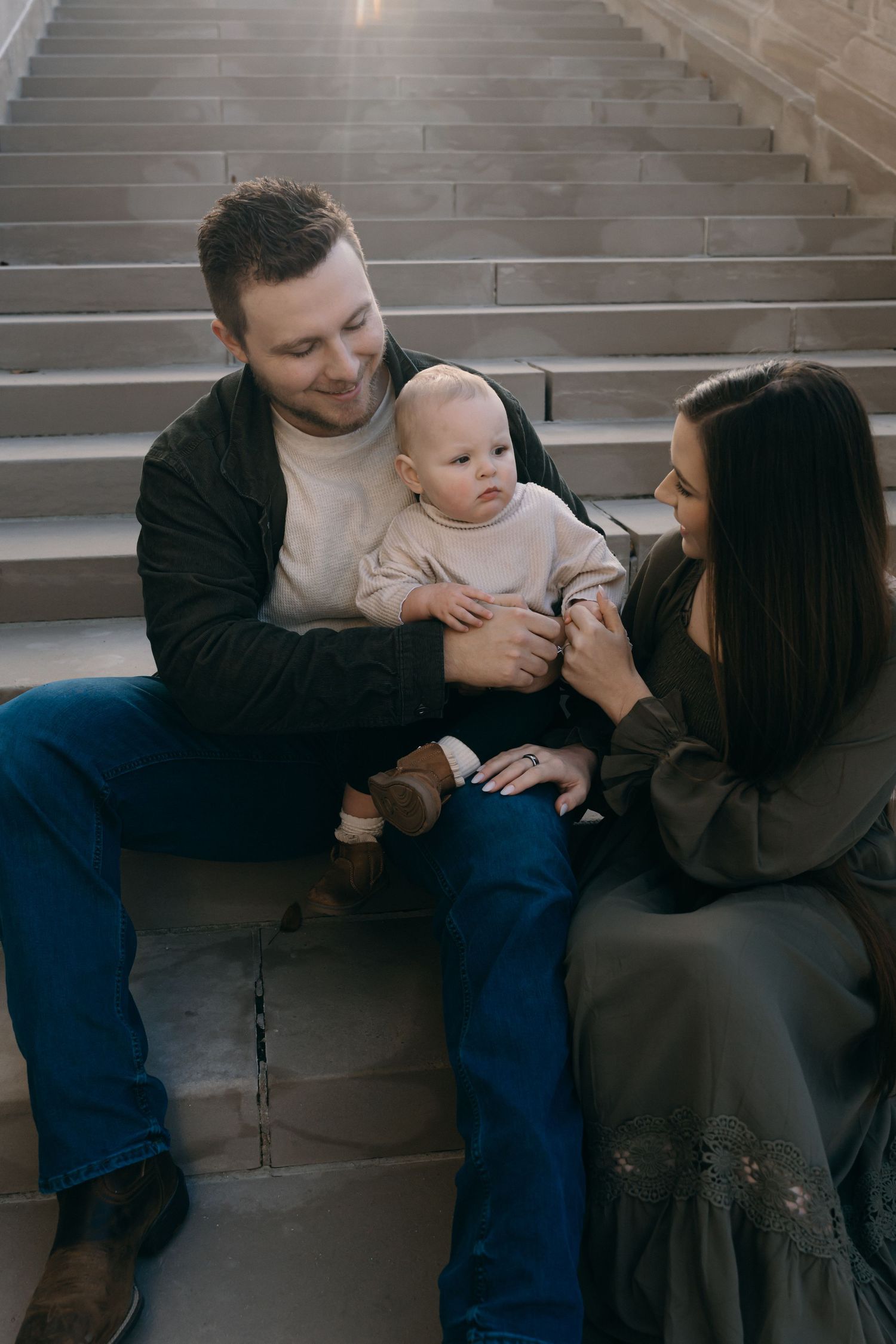 An intimate family portrait on grey concrete steps showing a tender moment with a baby.