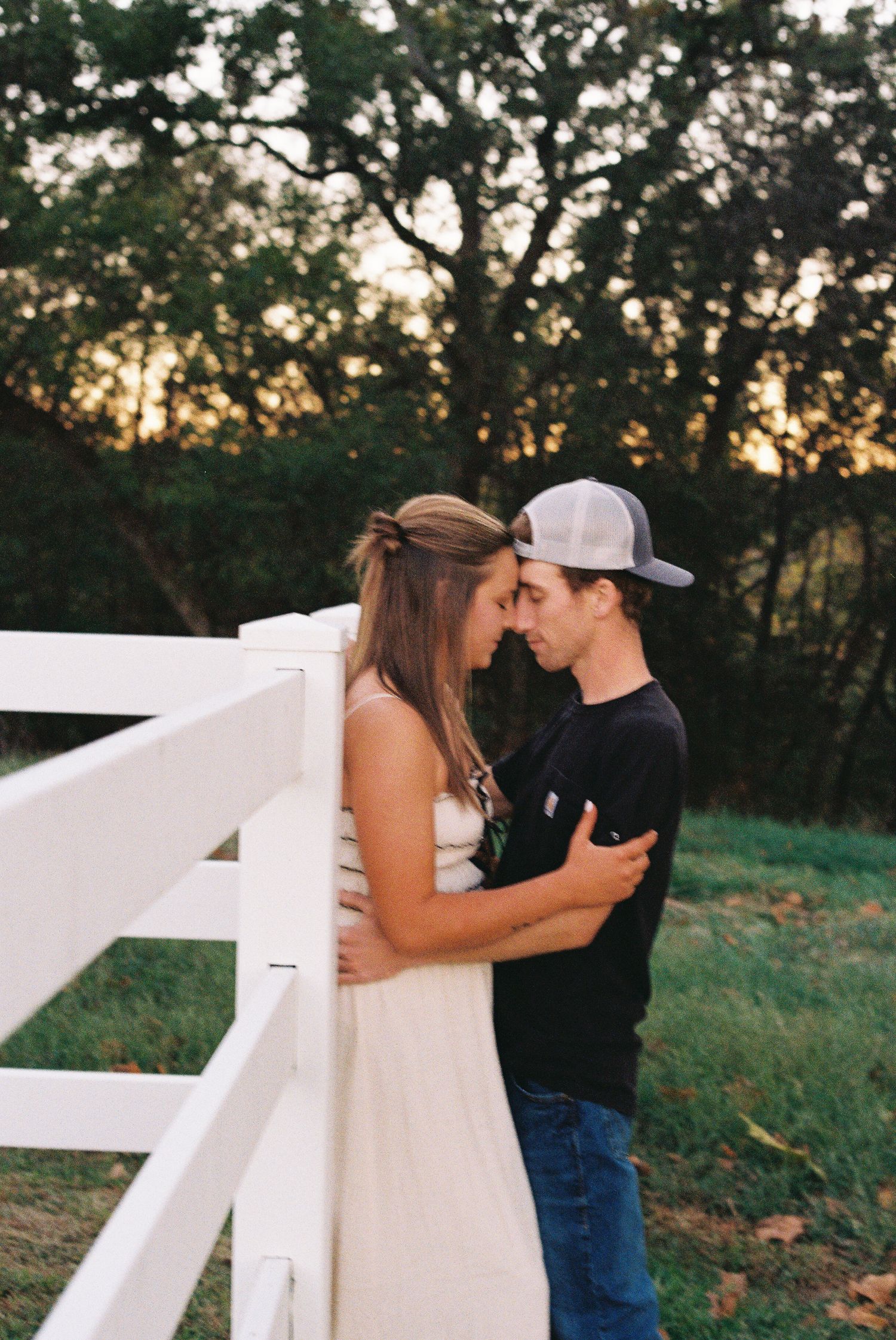 Romantic moment shared against white fence during golden hour.