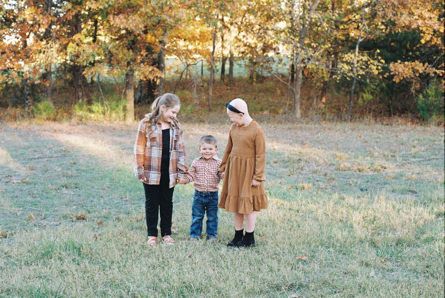 Three people standing together in misty autumn field at sunset.