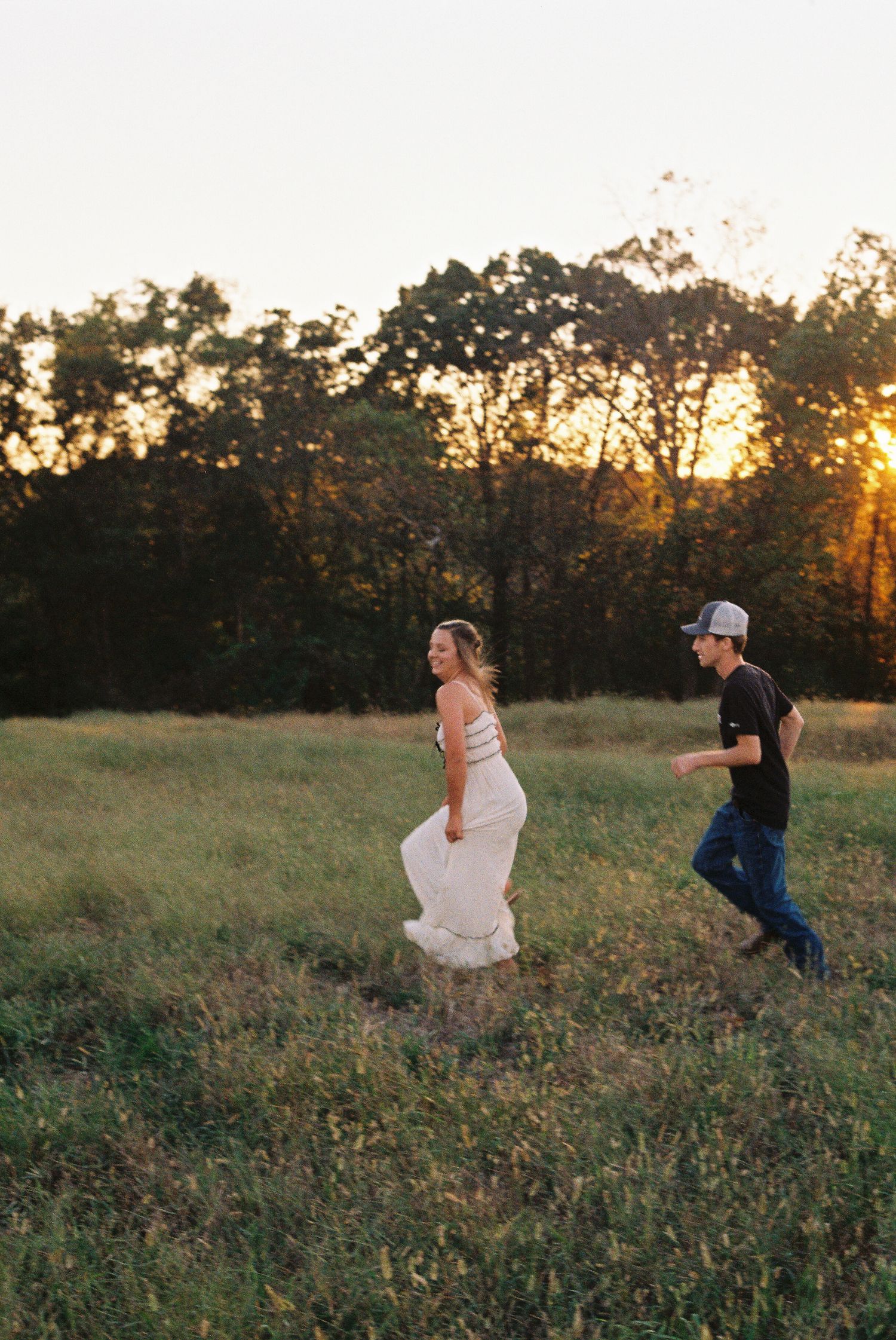 Playful couple running through a golden field at sunset.