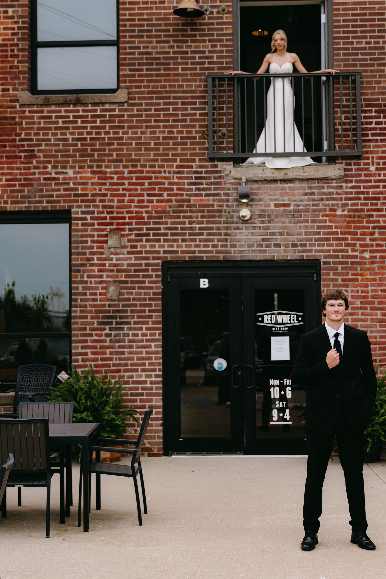 Wedding party members pose separately across brick building facade with outdoor furniture.