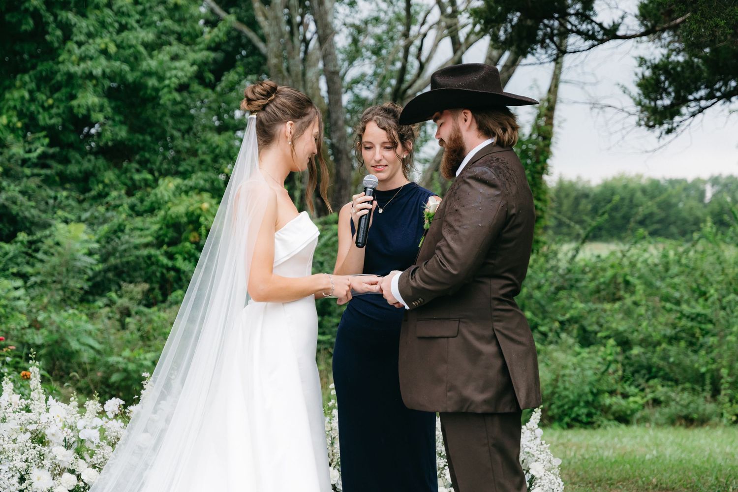 Outdoor wedding ceremony takes place against lush green backdrop.