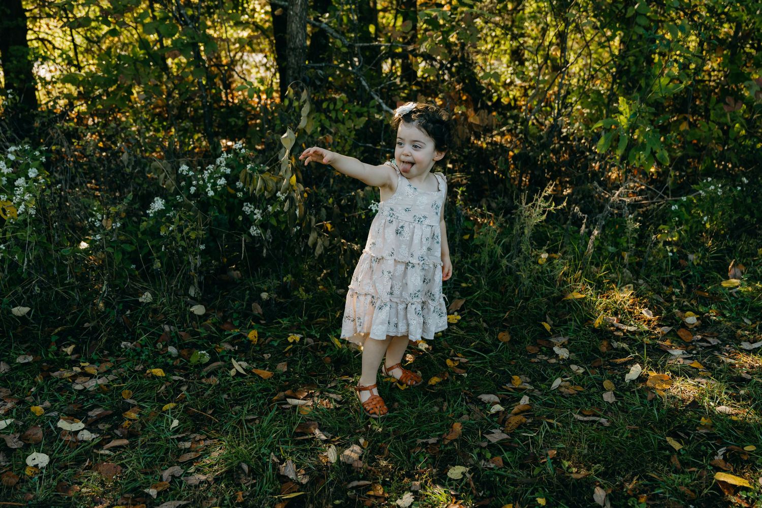 A child in a floral dress dances through fallen autumn leaves.
