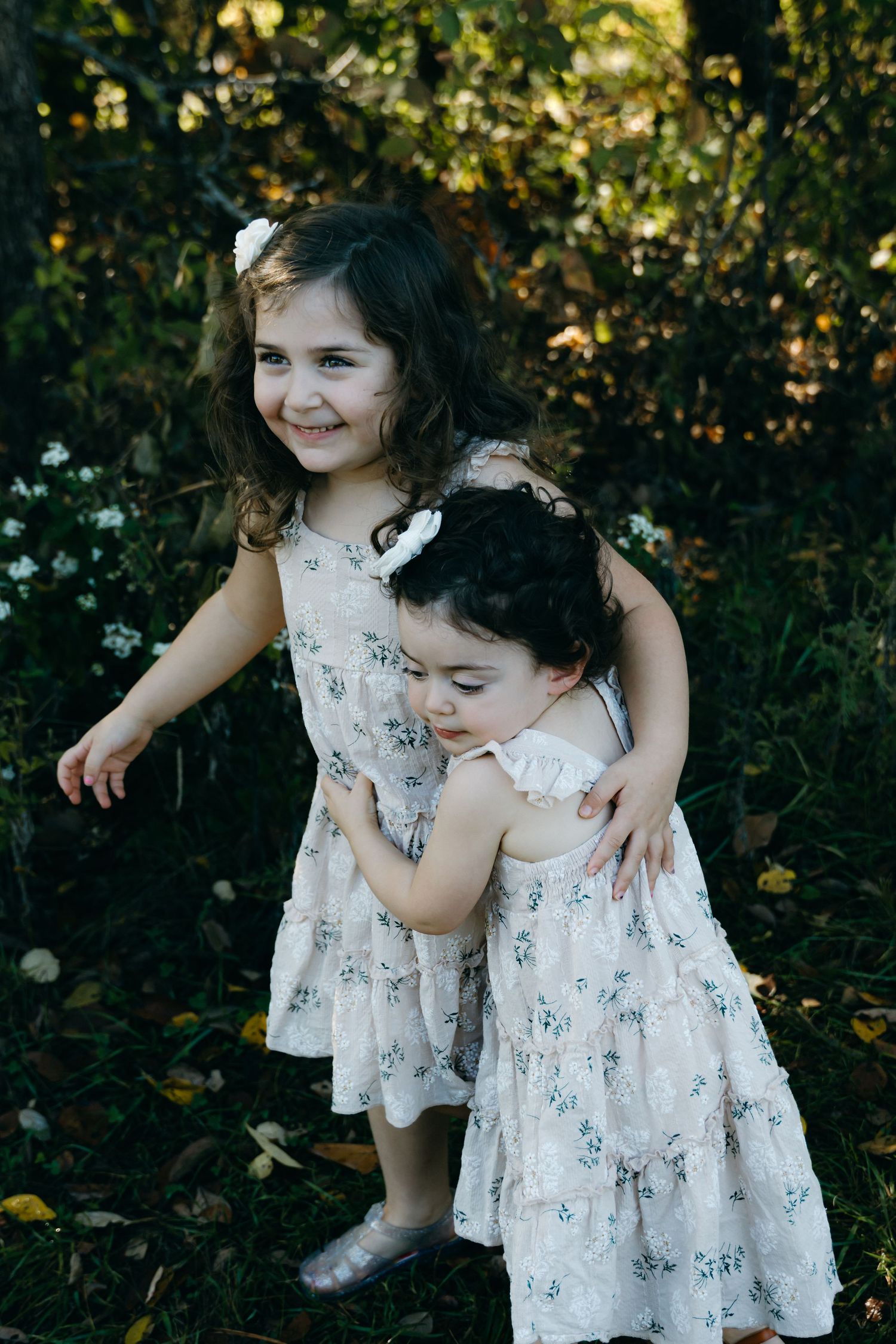 Two children in matching floral dresses play together outdoors.