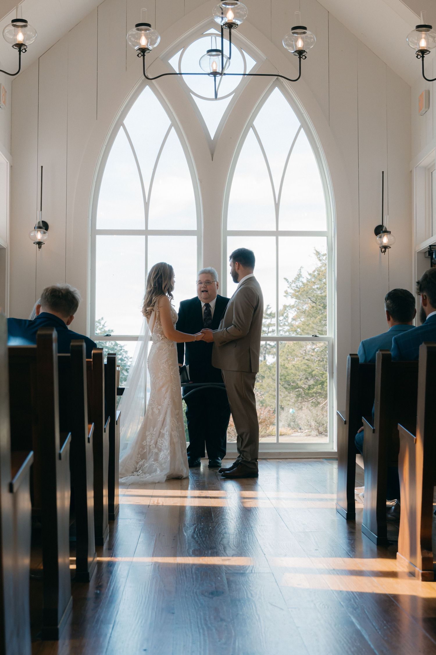 Wedding ceremony in a bright chapel with arched windows and wooden pews.