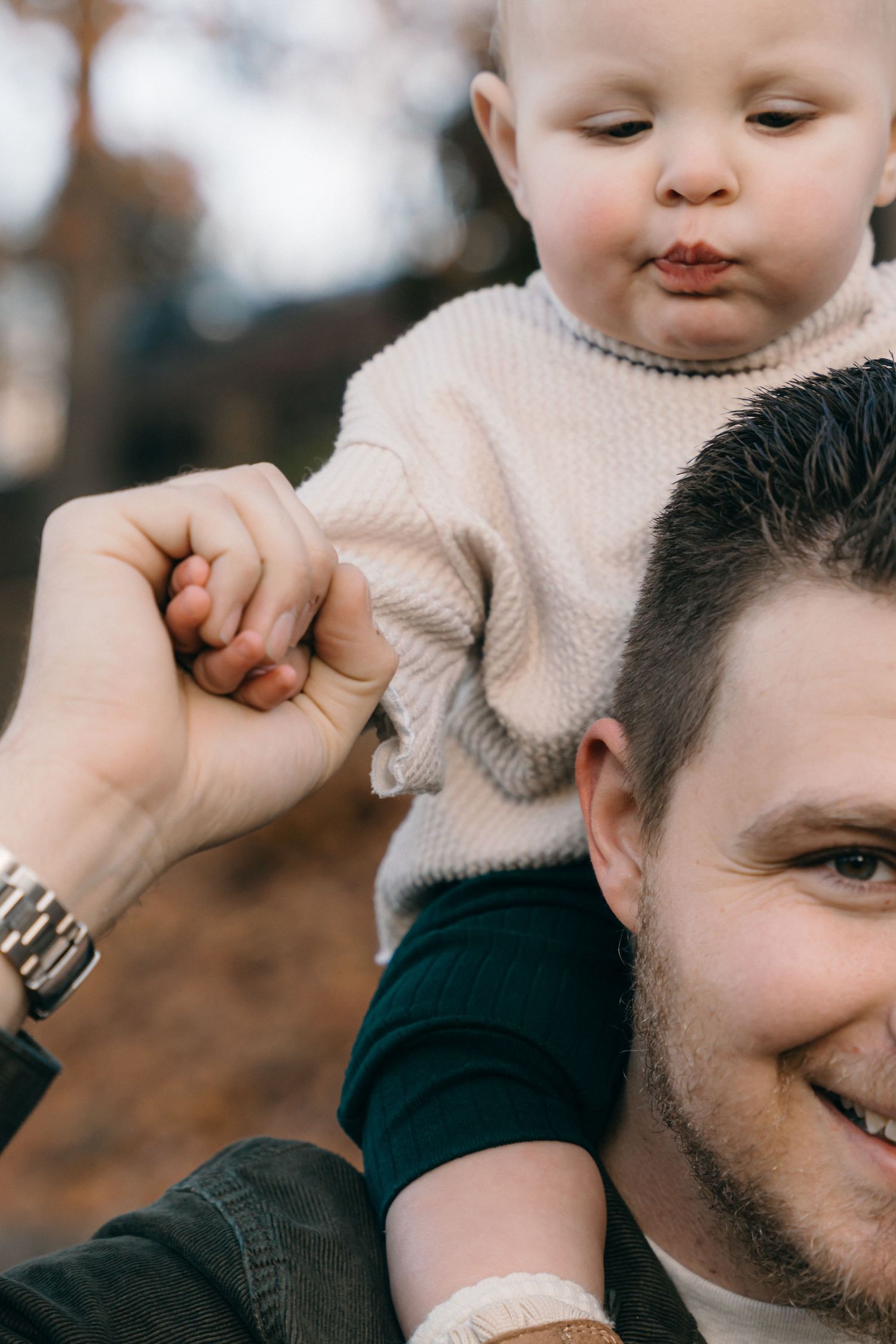 A close-up candid moment showing a baby in a cream sweater being held up.