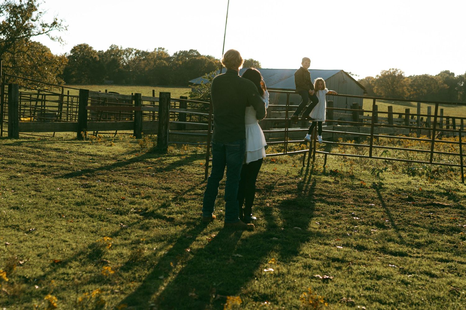 Silhouettes against sunset in a farm field with wooden fencing.