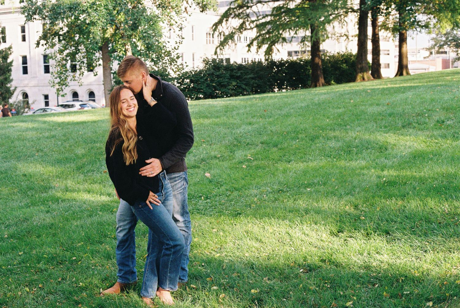 Couple shares intimate moment on grassy lawn near historic building.