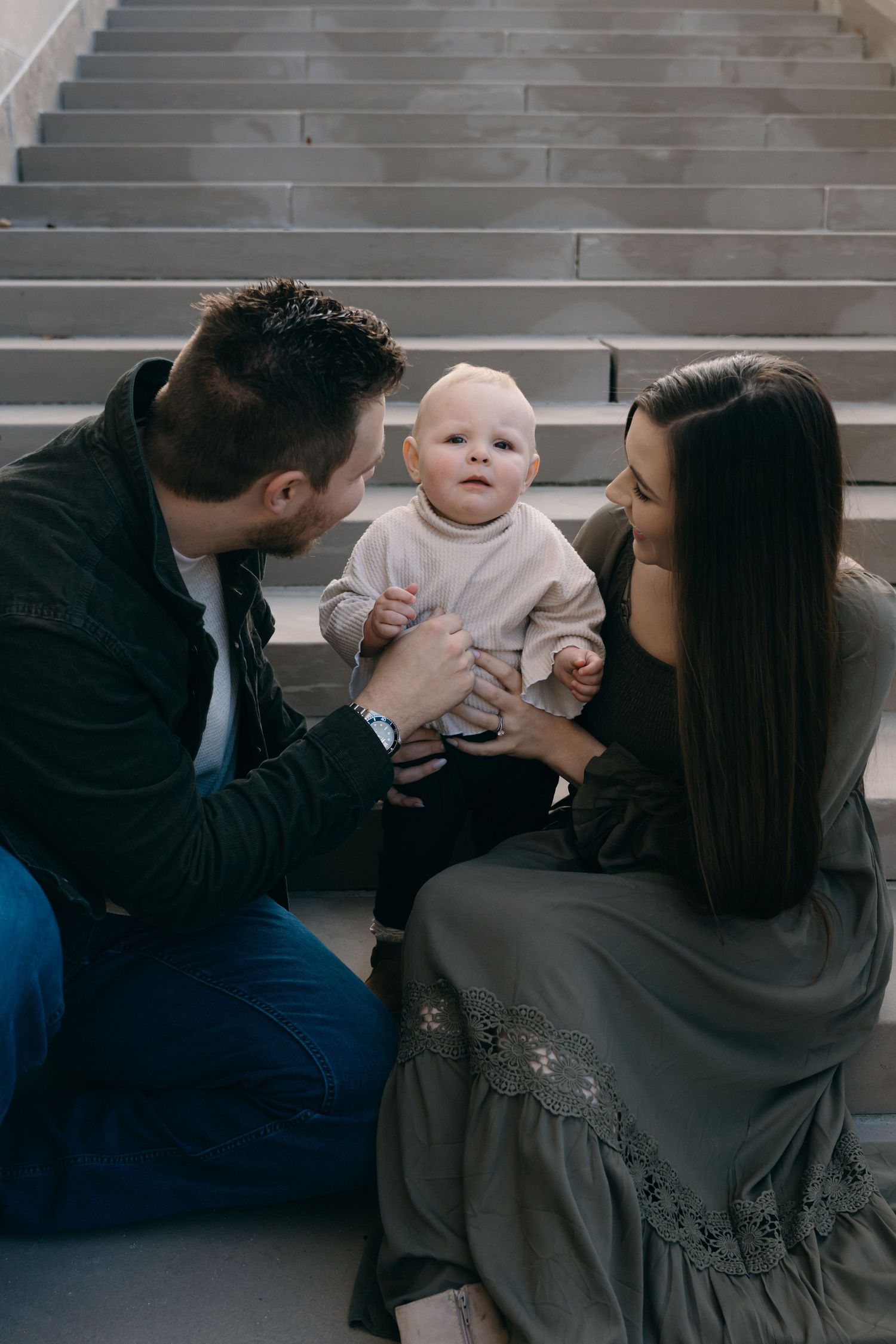 An intimate family moment captured on grey stairs with a baby in white.