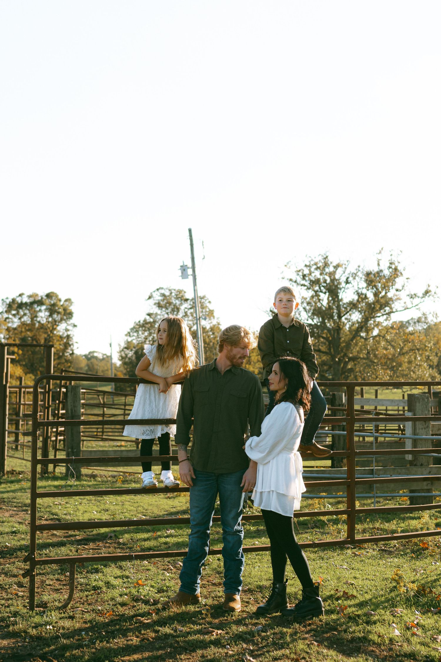 Family gathering at sunset near wooden fences on a rustic farm property.