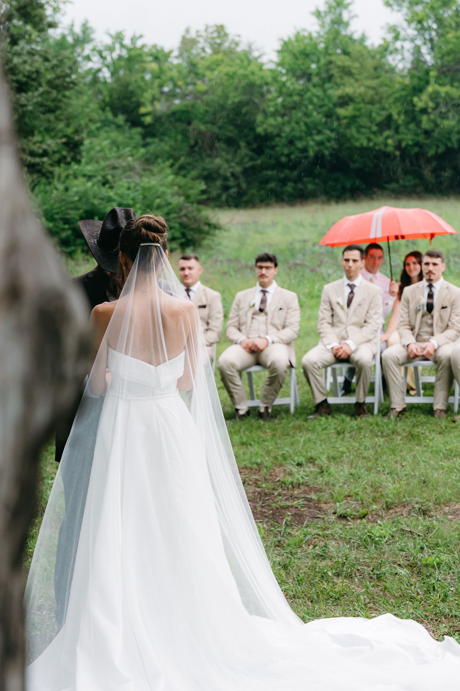 Elegant wedding dress train flows across grass with guests seated in background.
